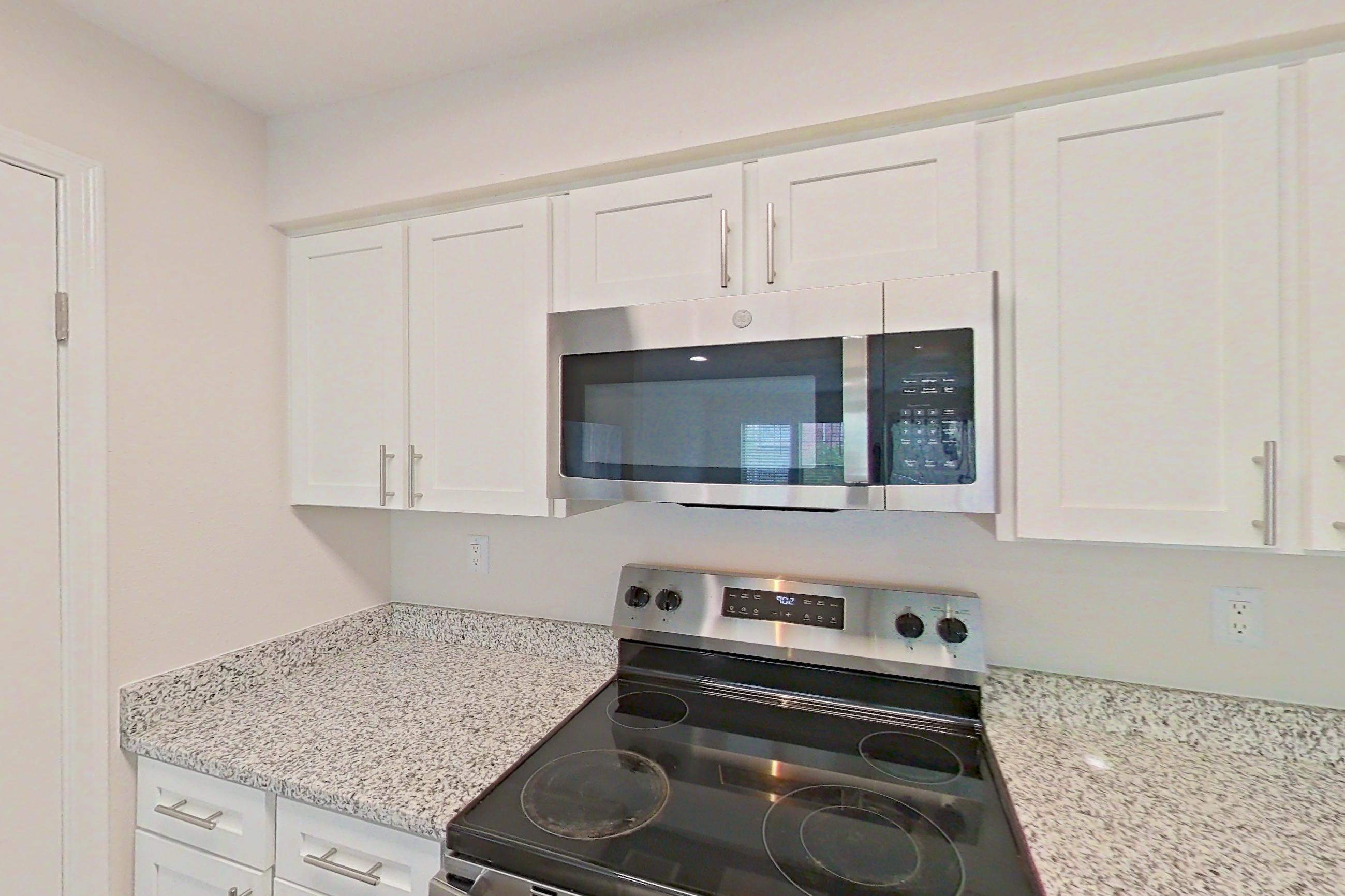 Kitchen with dishwasher, electric range, fireplace, light countertops, light stone countertops, light wood-finish flooring, microwave, oven/range, refrigerator, stainless steel appliances, and white appliances, Apartment 5117 at Cortland Van Dorn