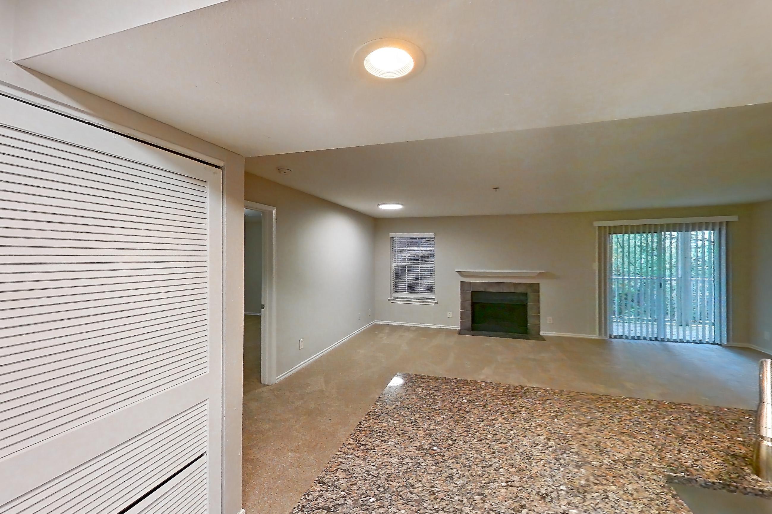 Kitchen with dark stone countertops, dishwasher, electric range, fireplace, light countertops, light wood-finish flooring, microwave, oven/range, refrigerator, stainless steel appliances, and tile fireplace, Apartment 2207 at Cortland Van Dorn