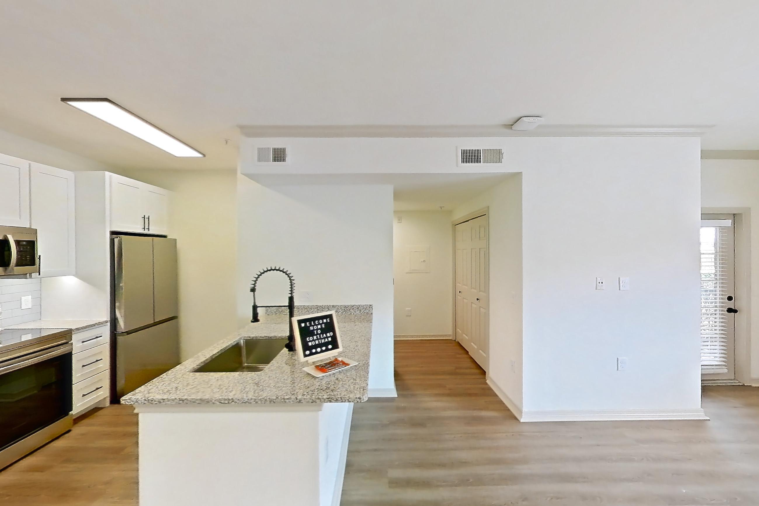 Living space with electric range, light stone countertops, light wood-finish flooring, oven/range, refrigerator, and stainless steel appliances, Apartment 4107 at Cortland Wortham