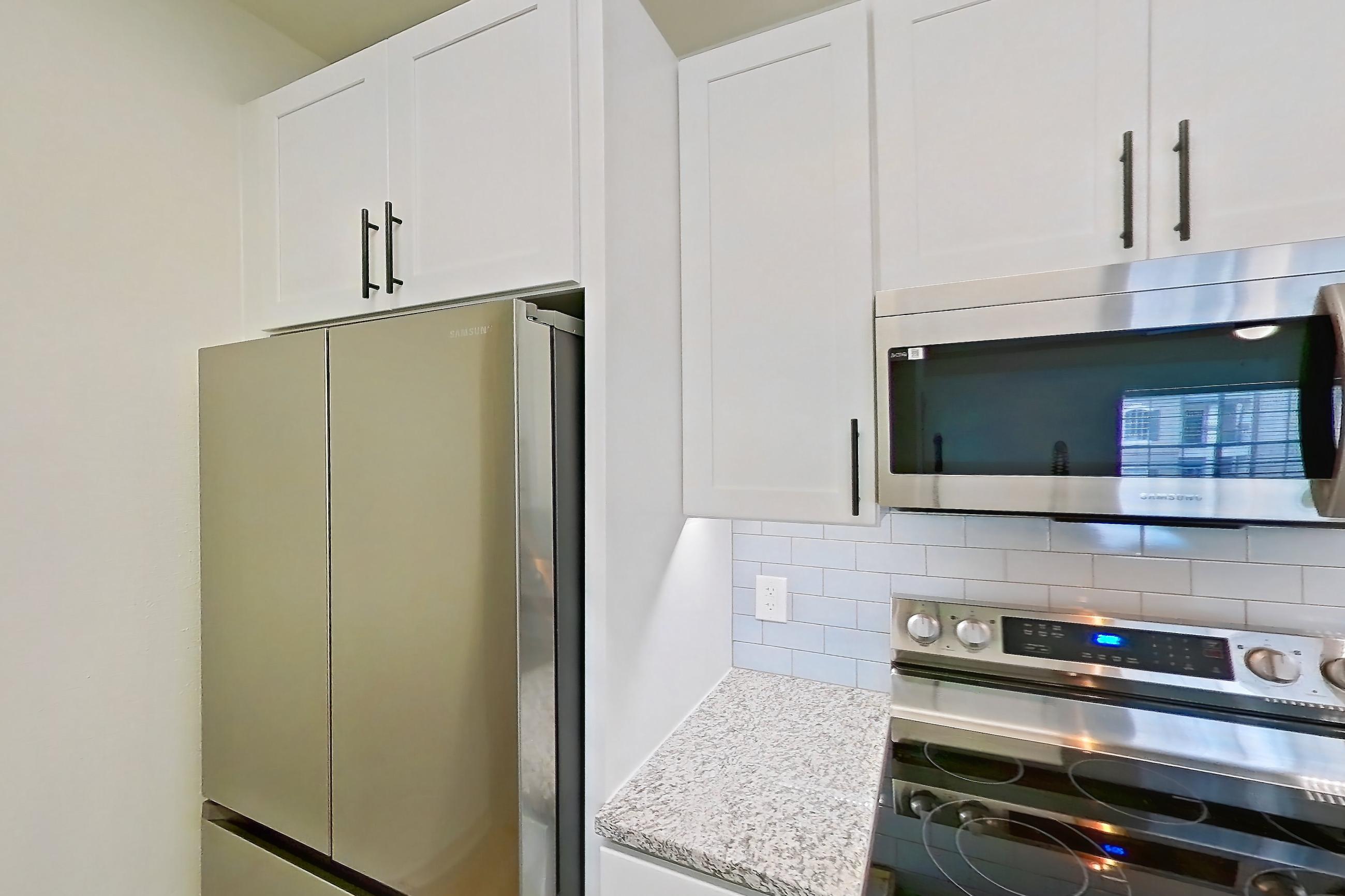 Kitchen with dishwasher, electric range, light countertops, light stone countertops, light wood-finish flooring, microwave, oven/range, stainless steel appliances, and white appliances, Apartment 5209 at Cortland Wortham