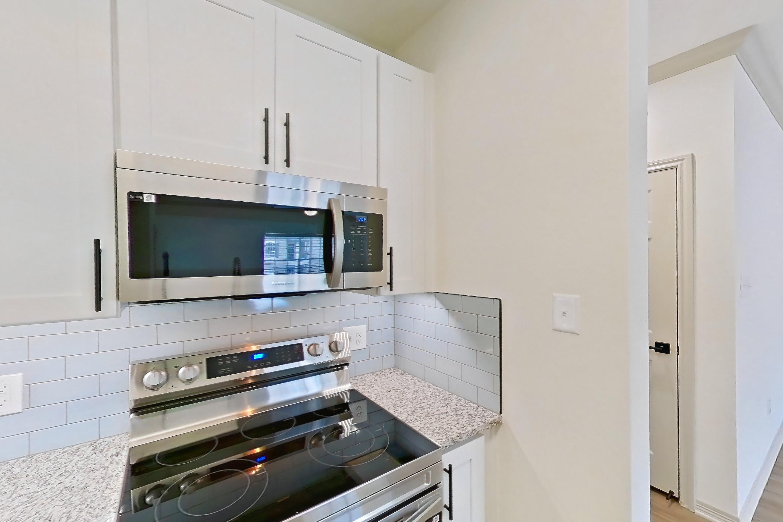Kitchen with dishwasher, electric range, light countertops, light stone countertops, light wood-finish flooring, microwave, oven/range, stainless steel appliances, and white appliances, Apartment 5209 at Cortland Wortham