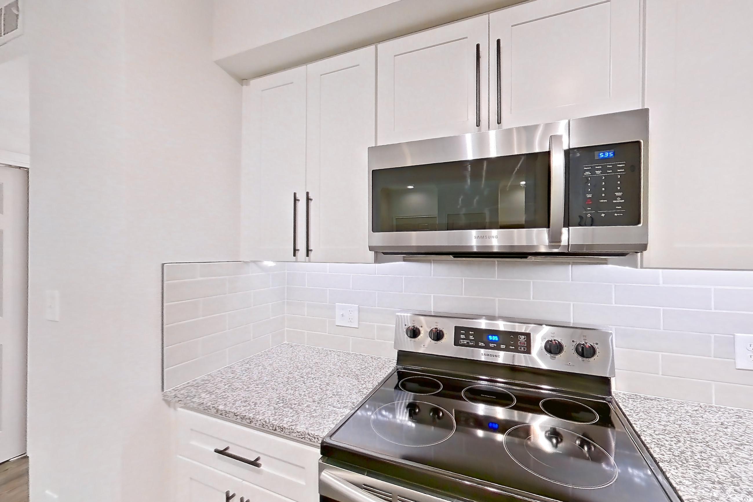 Kitchen with dark wood-finish flooring, dishwasher, electric range, light countertops, light stone countertops, light wood-finish flooring, oven/range, refrigerator, and stainless steel appliances, Apartment 2304 at Cortland at Twin Creeks