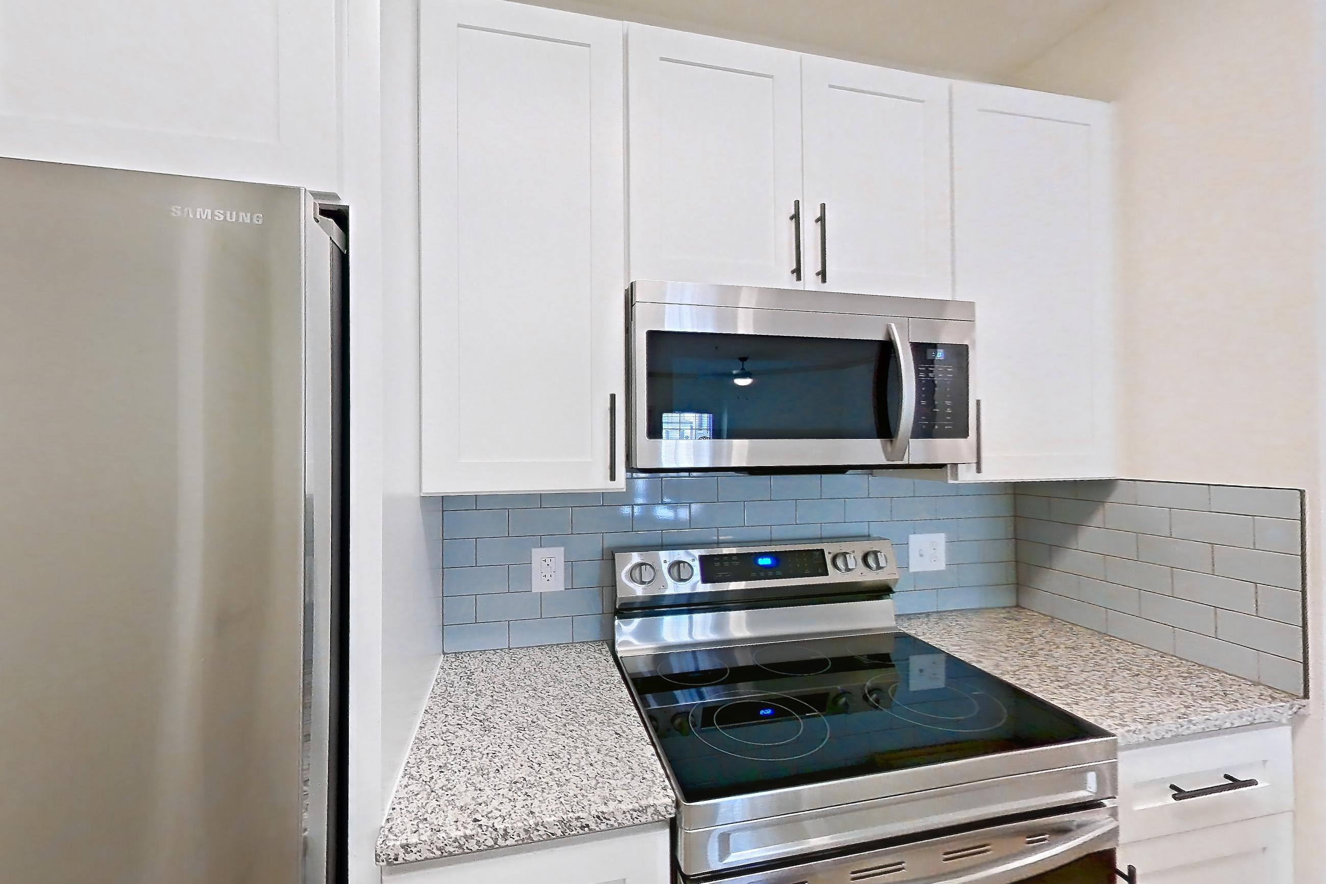 Kitchen with dishwasher, electric range, light countertops, light stone countertops, light wood-finish flooring, microwave, oven/range, and stainless steel appliances, Apartment 17210 at Cortland Wortham