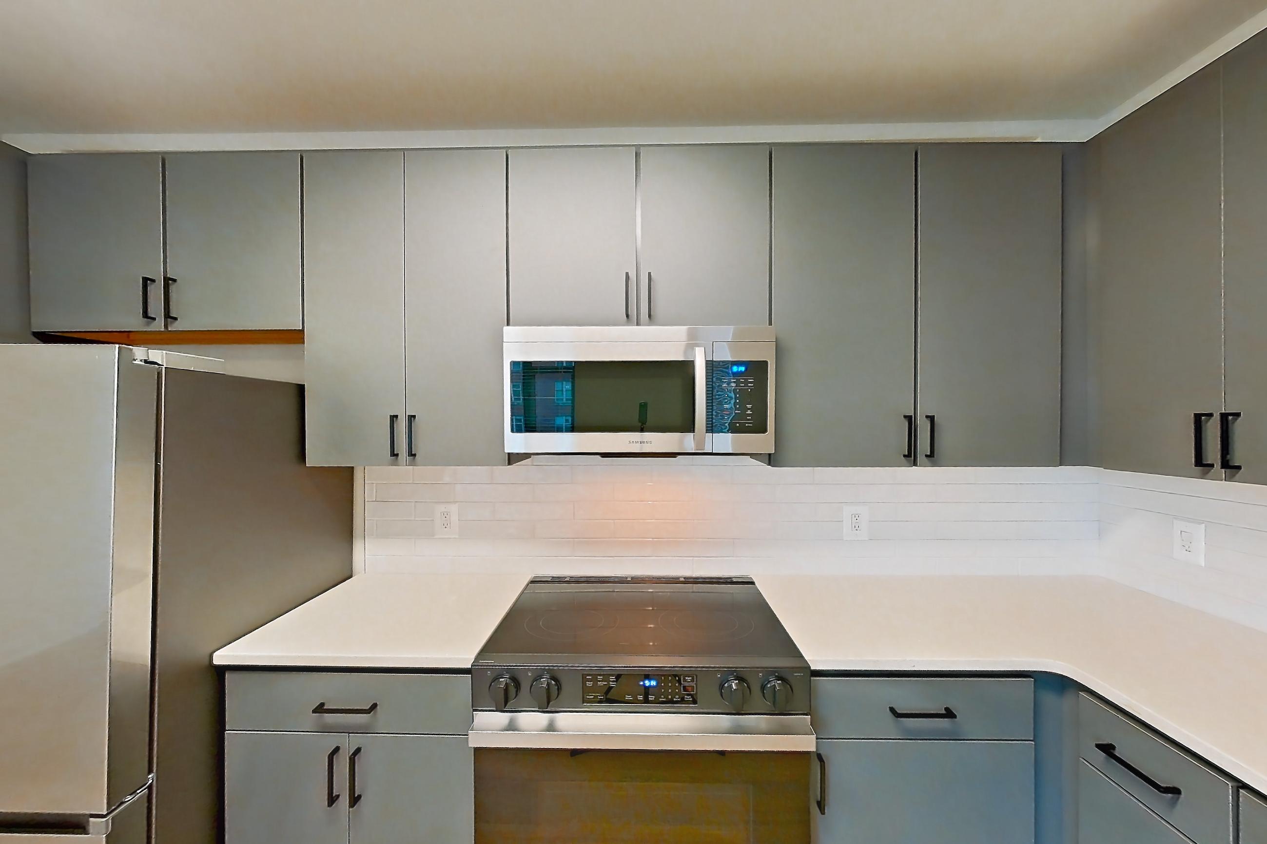 Kitchen with dishwasher, electric range, light countertops, light stone countertops, light wood-finish flooring, microwave, oven/range, refrigerator, and stainless steel appliances, Apartment 423 at Cortland Ballston