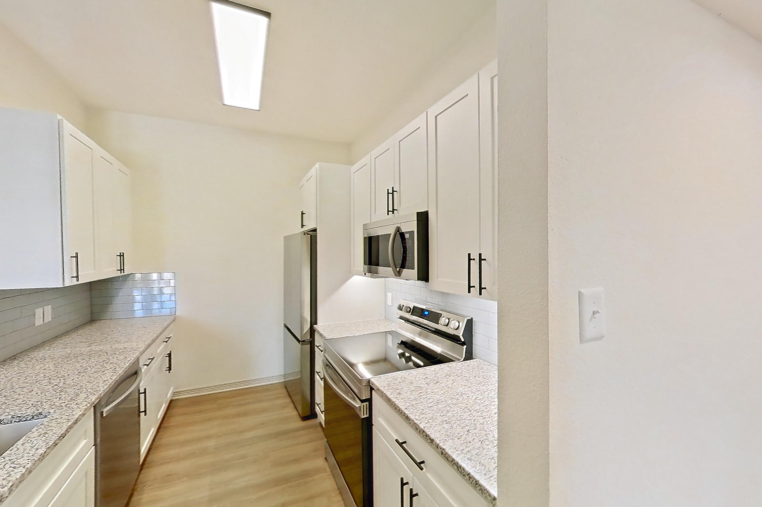 Kitchen space with dishwasher, electric range, light countertops, light stone countertops, light wood-finish flooring, microwave, oven/range, refrigerator, and stainless steel appliances, Apartment 8305 at Cortland Wortham