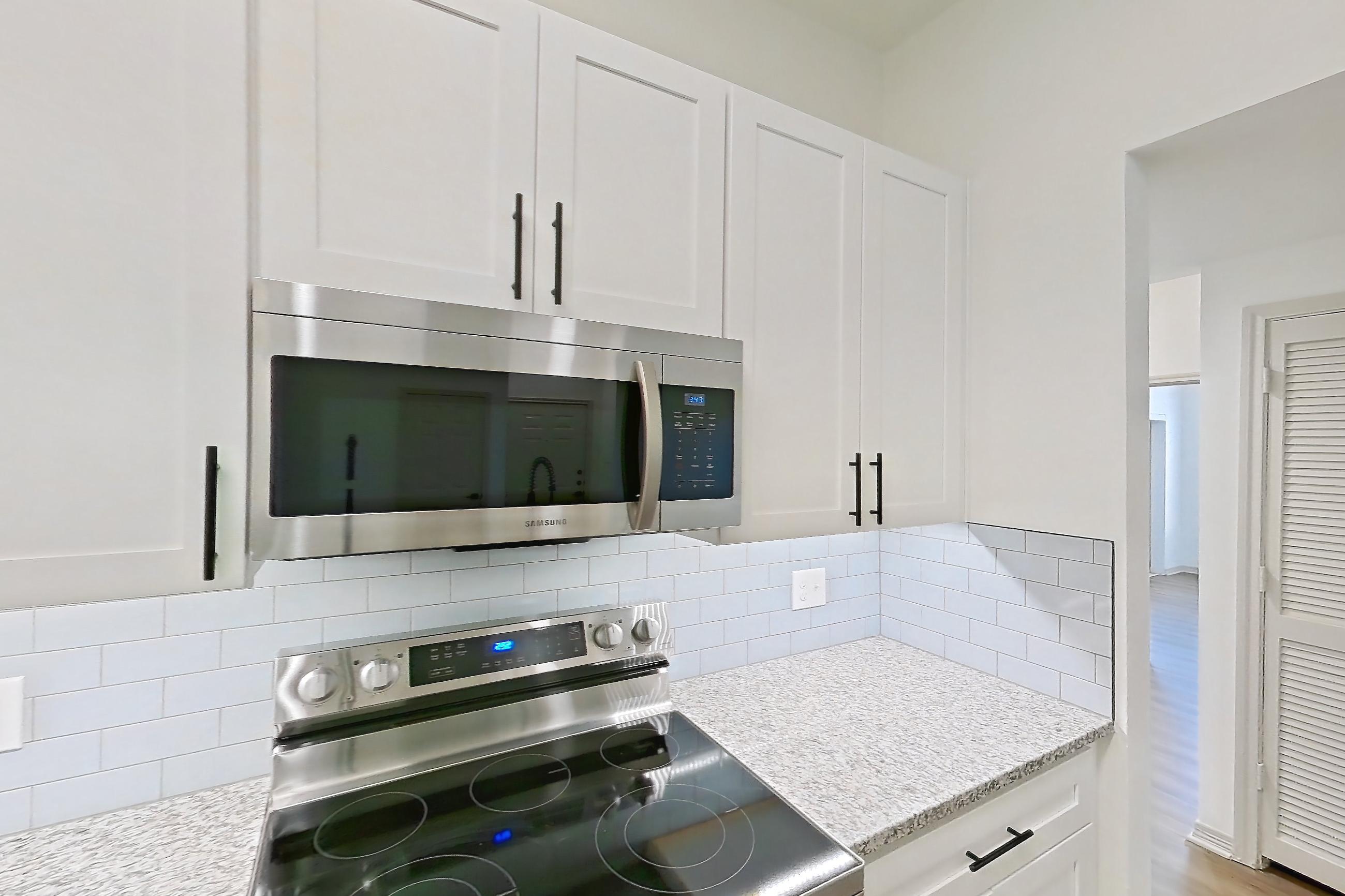 Kitchen with dishwasher, electric range, light countertops, light stone countertops, light wood-finish flooring, microwave, oven/range, refrigerator, and stainless steel appliances, Apartment 8305 at Cortland Wortham