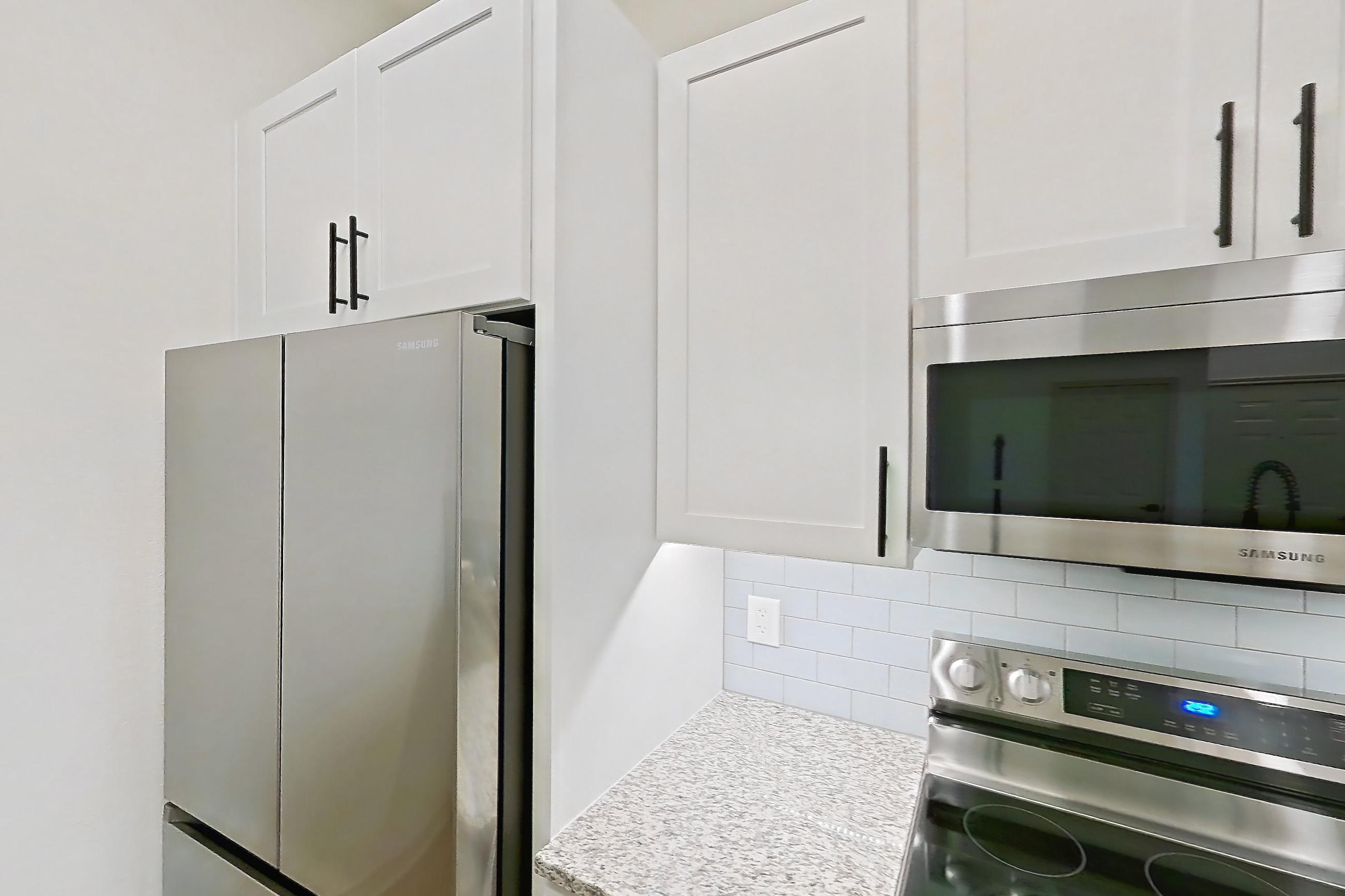 Kitchen with dishwasher, electric range, light countertops, light stone countertops, light wood-finish flooring, microwave, oven/range, refrigerator, and stainless steel appliances, Apartment 8305 at Cortland Wortham
