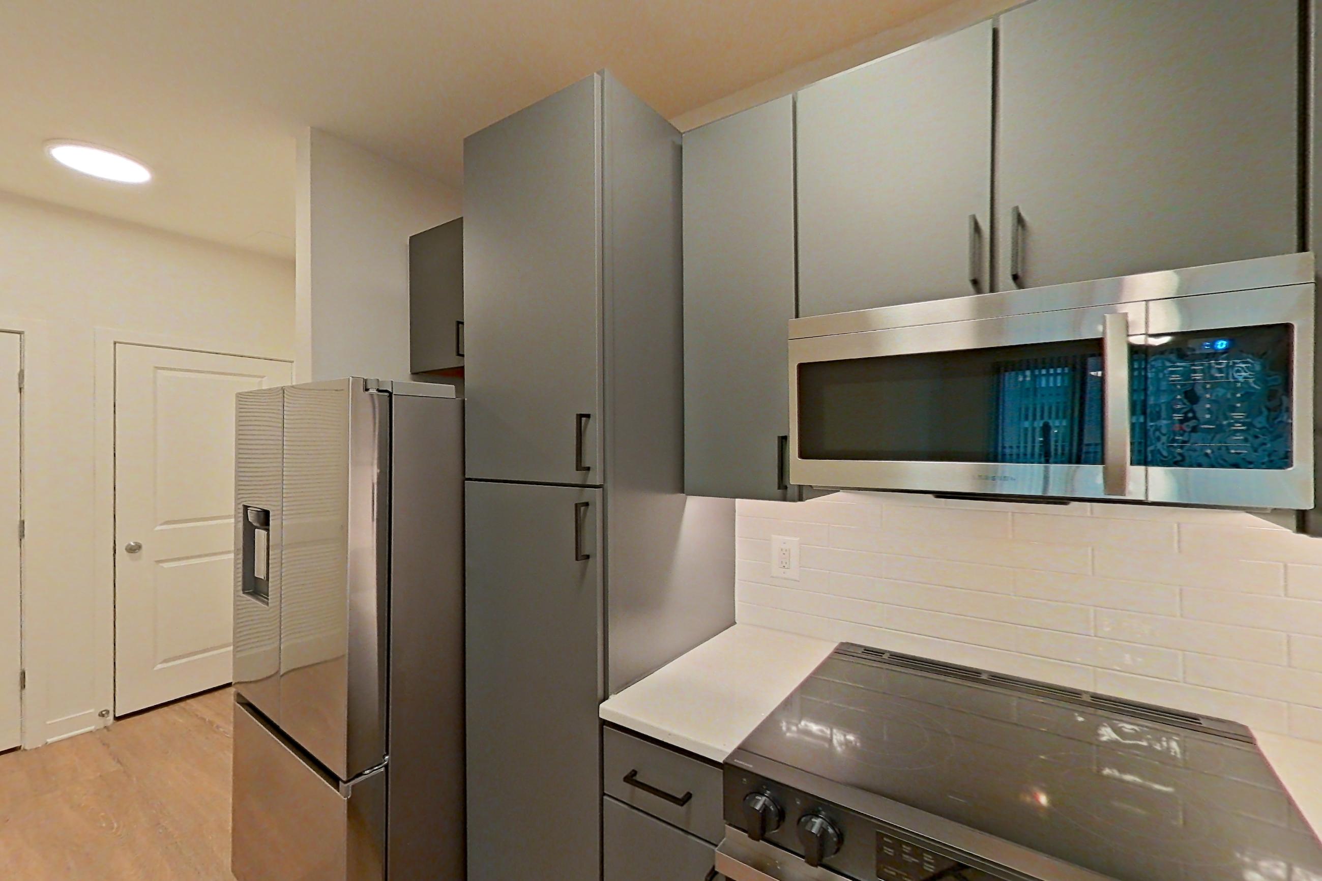 Kitchen with dishwasher, electric range, light countertops, light stone countertops, light wood-finish flooring, microwave, oven/range, and stainless steel appliances, Apartment 207 at Cortland Ballston