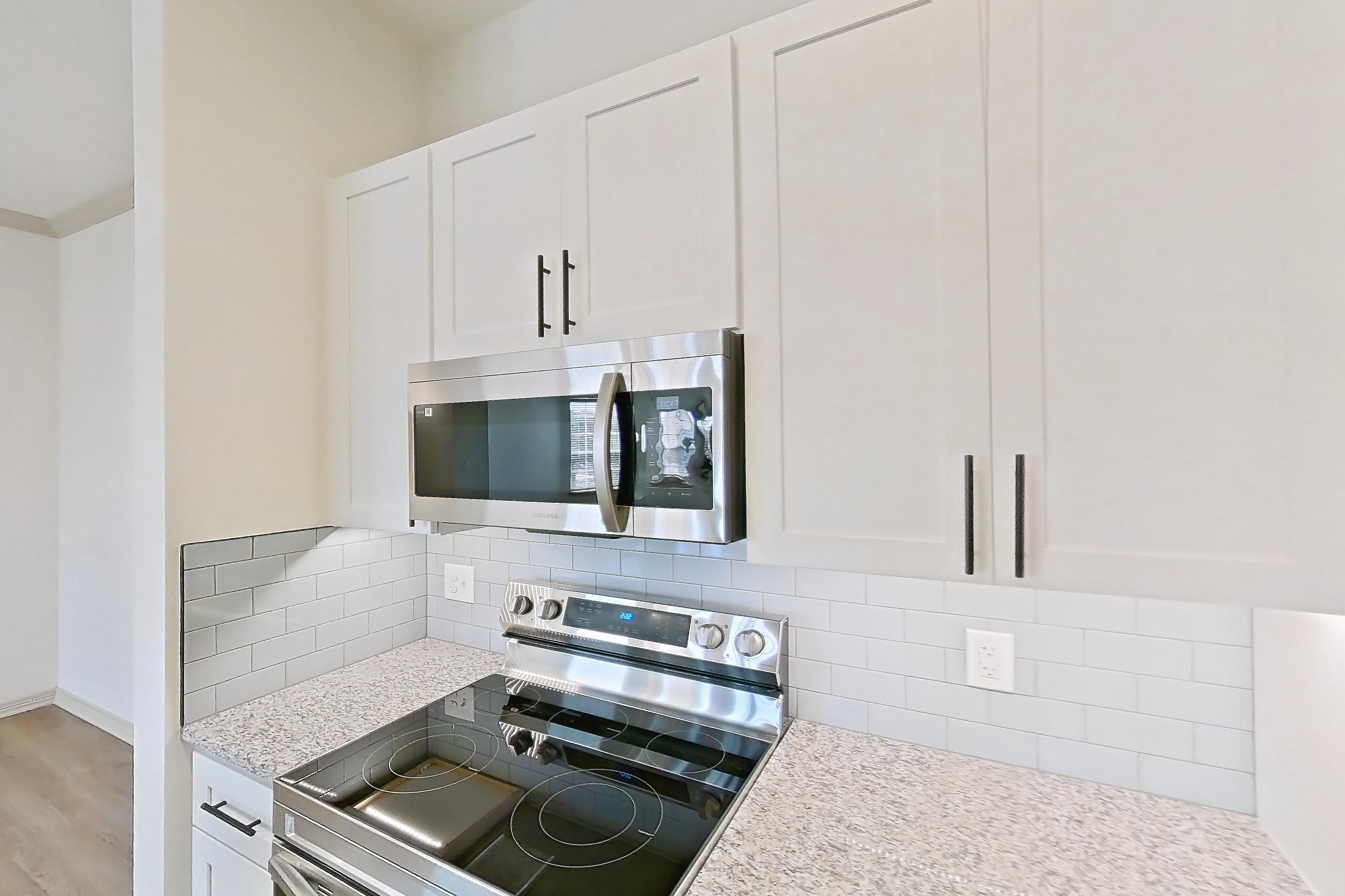 Kitchen with dishwasher, electric range, light countertops, light stone countertops, light wood-finish flooring, microwave, oven/range, and stainless steel appliances, Apartment 2306 at Cortland Wortham