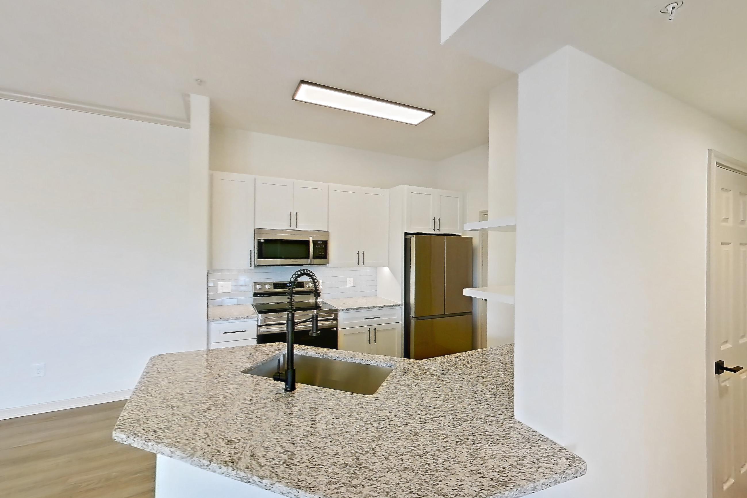 Living space with electric range, kitchen island, light countertops, light stone countertops, light wood-finish flooring, oven/range, refrigerator, and stainless steel appliances, Apartment 2306 at Cortland Wortham
