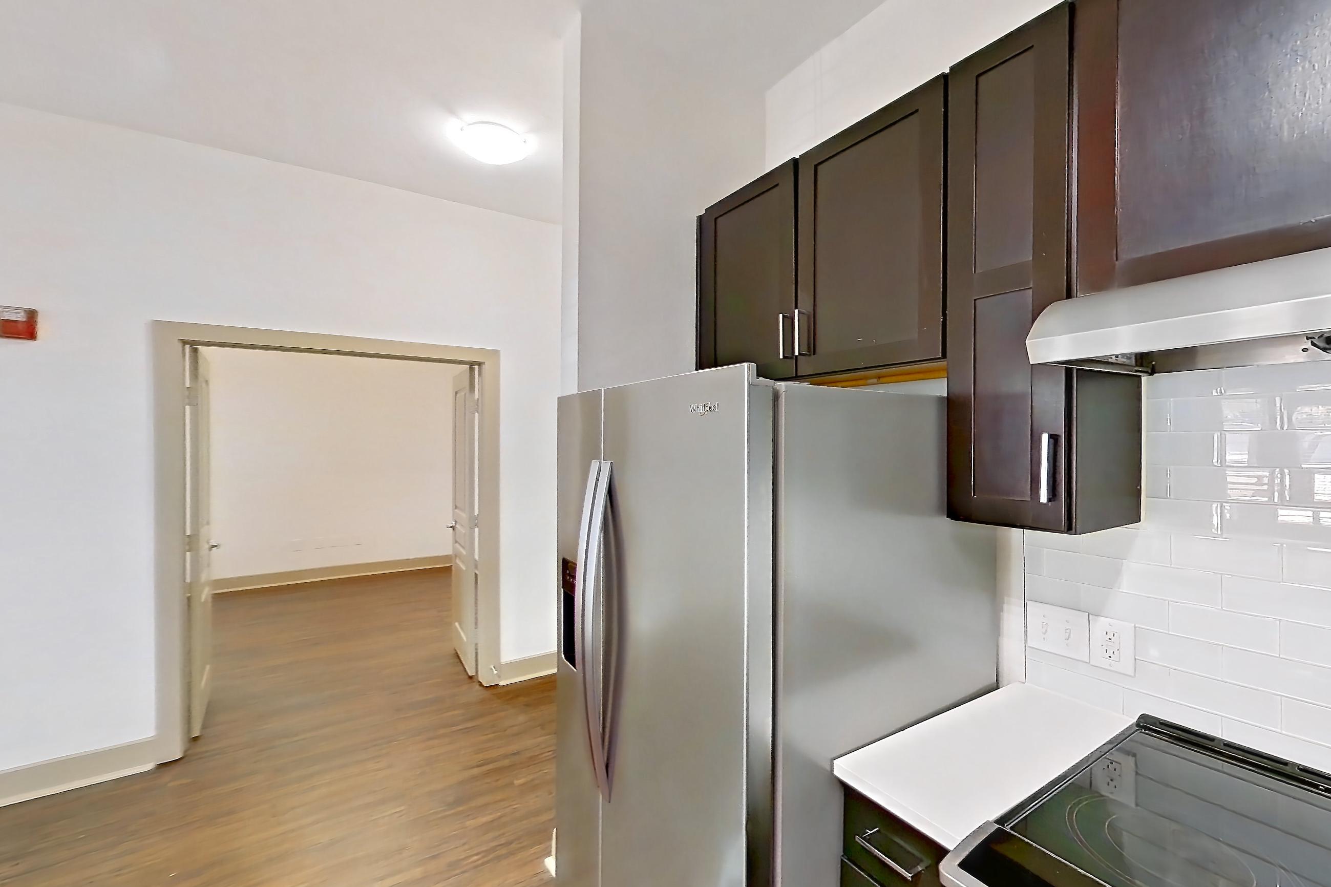Kitchen with dark wood-finish flooring, dishwasher, light countertops, microwave, refrigerator, stainless steel appliances, and water & ice dispenser, Apartment 3114 at Cortland Galleria