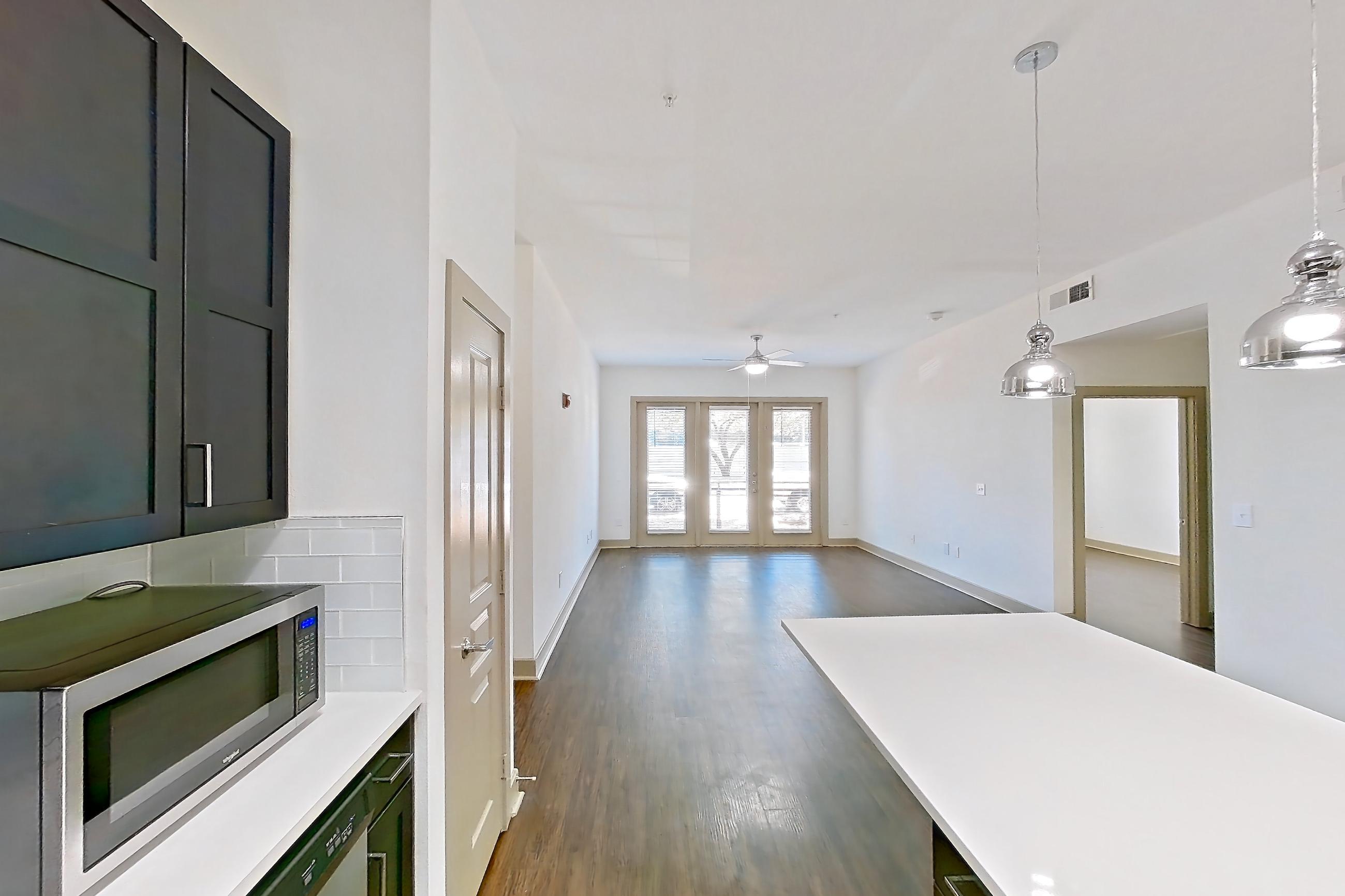 Kitchen with dark wood-finish flooring, dishwasher, light countertops, microwave, refrigerator, stainless steel appliances, and water & ice dispenser, Apartment 3114 at Cortland Galleria