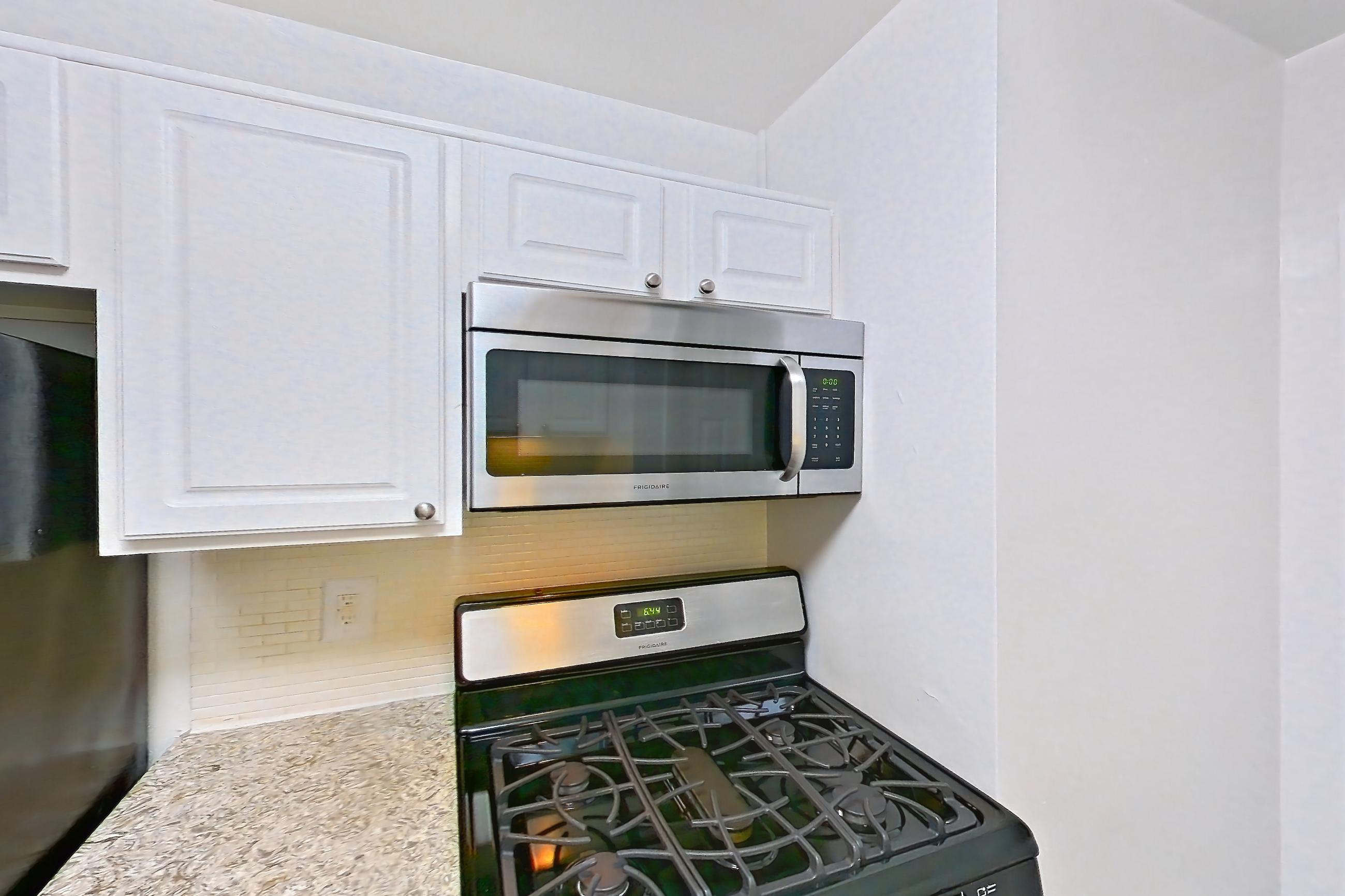 Kitchen with dark wood-finish flooring, dishwasher, gas range, light countertops, light stone countertops, microwave, oven/range, refrigerator, and stainless steel appliances, Apartment S-803 at Cortland on Pike
