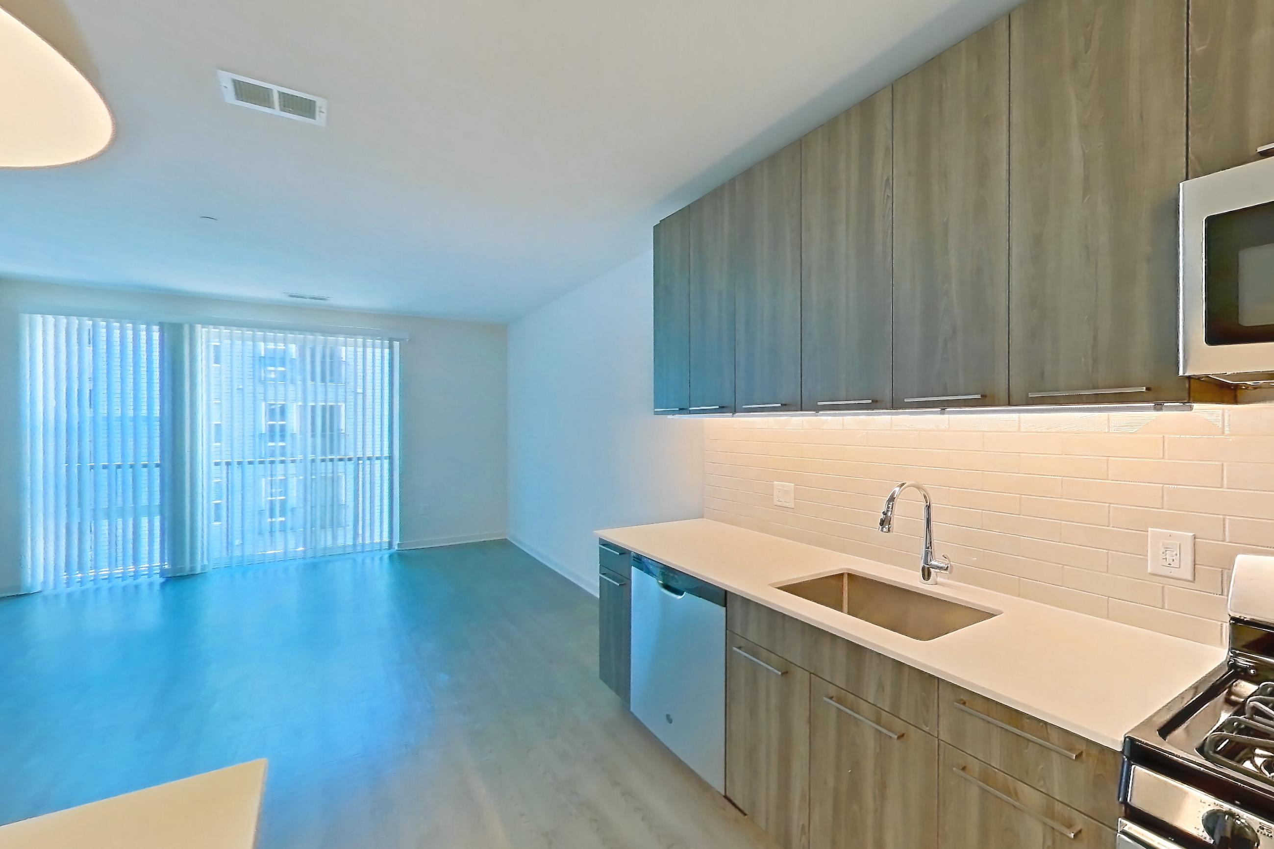 Kitchen with dishwasher, gas range, light countertops, light stone countertops, light wood-finish flooring, microwave, oven/range, refrigerator, and stainless steel appliances, Apartment 565 at Cortland Columbia Pike