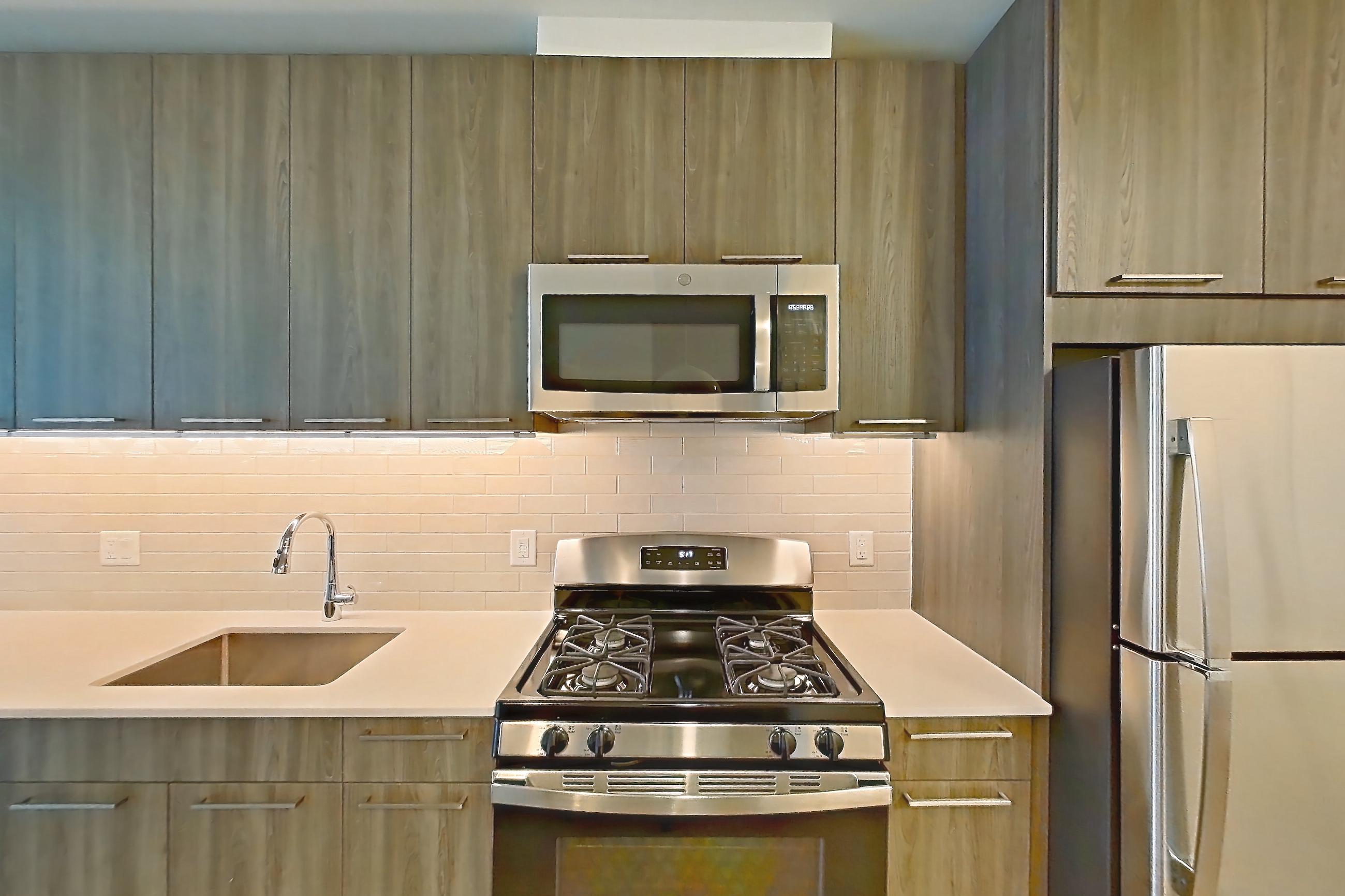 Kitchen with dishwasher, gas range, light countertops, light stone countertops, light wood-finish flooring, microwave, oven/range, refrigerator, and stainless steel appliances, Apartment 565 at Cortland Columbia Pike