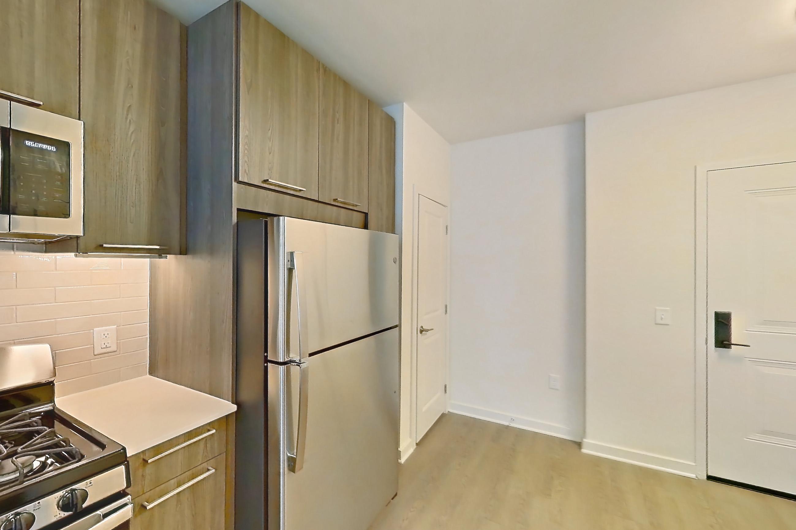 Kitchen with dishwasher, gas range, light countertops, light stone countertops, light wood-finish flooring, microwave, oven/range, refrigerator, and stainless steel appliances, Apartment 565 at Cortland Columbia Pike
