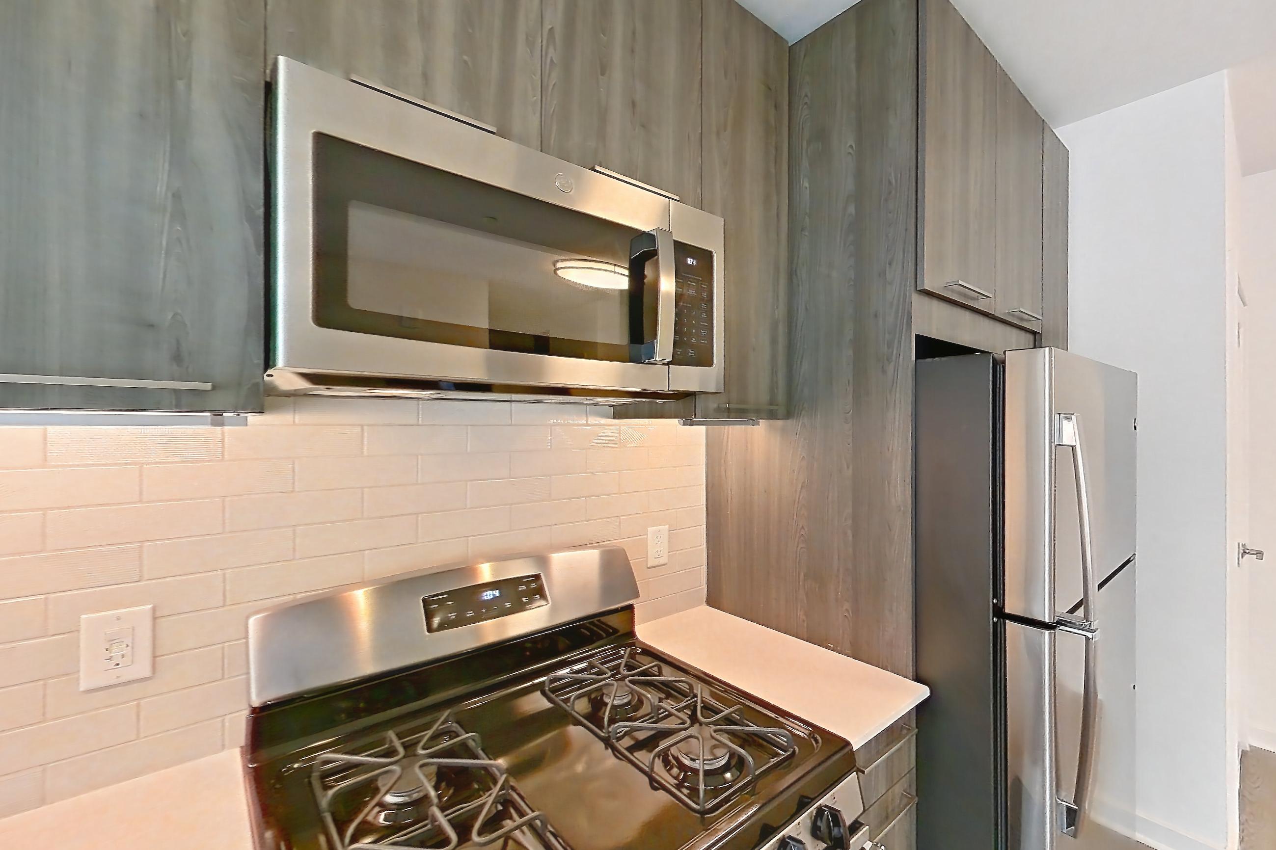 Kitchen with dishwasher, gas range, light stone countertops, light wood-finish flooring, microwave, oven/range, and stainless steel appliances, Apartment 159 at Cortland Columbia Pike
