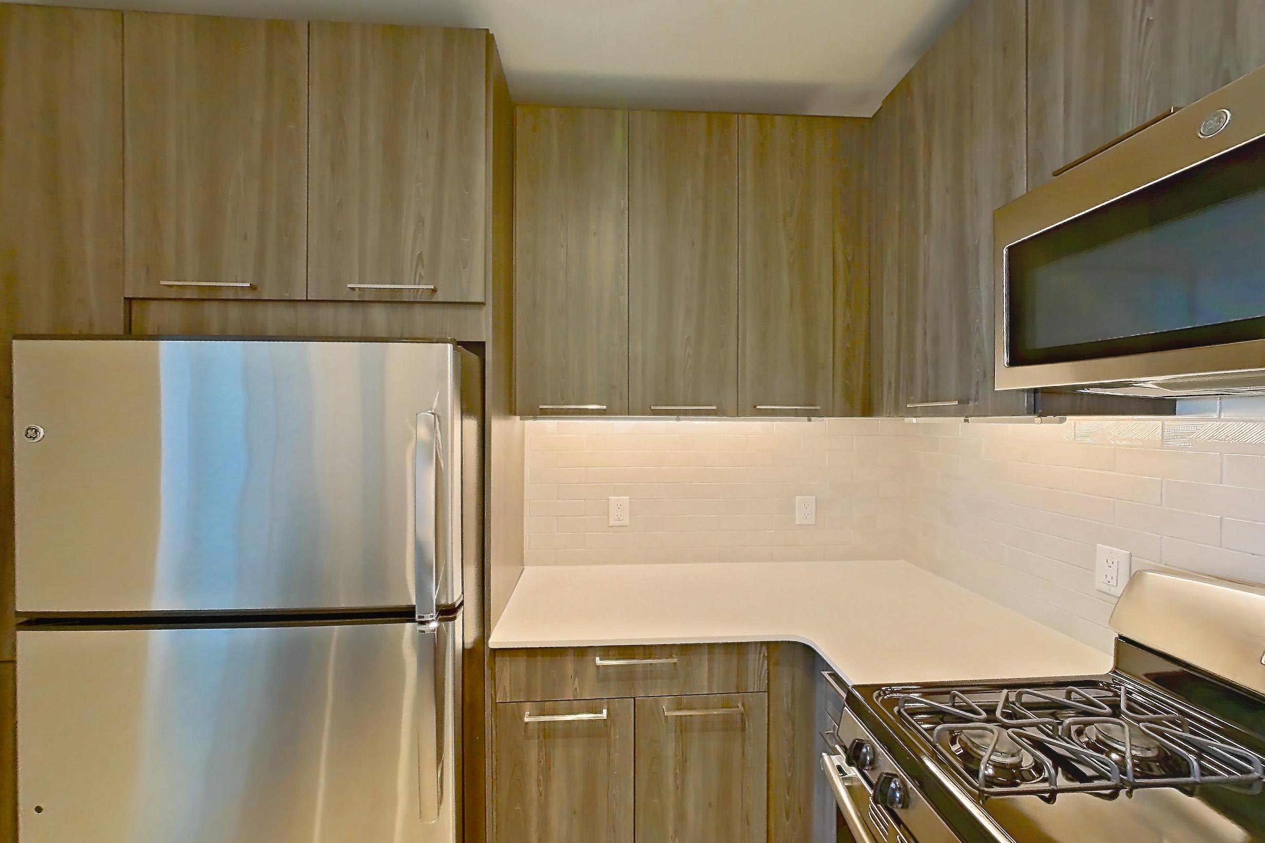 Kitchen with gas range, light countertops, light stone countertops, light wood-finish flooring, microwave, oven/range, refrigerator, and stainless steel appliances, Apartment 633S at Cortland Columbia Pike