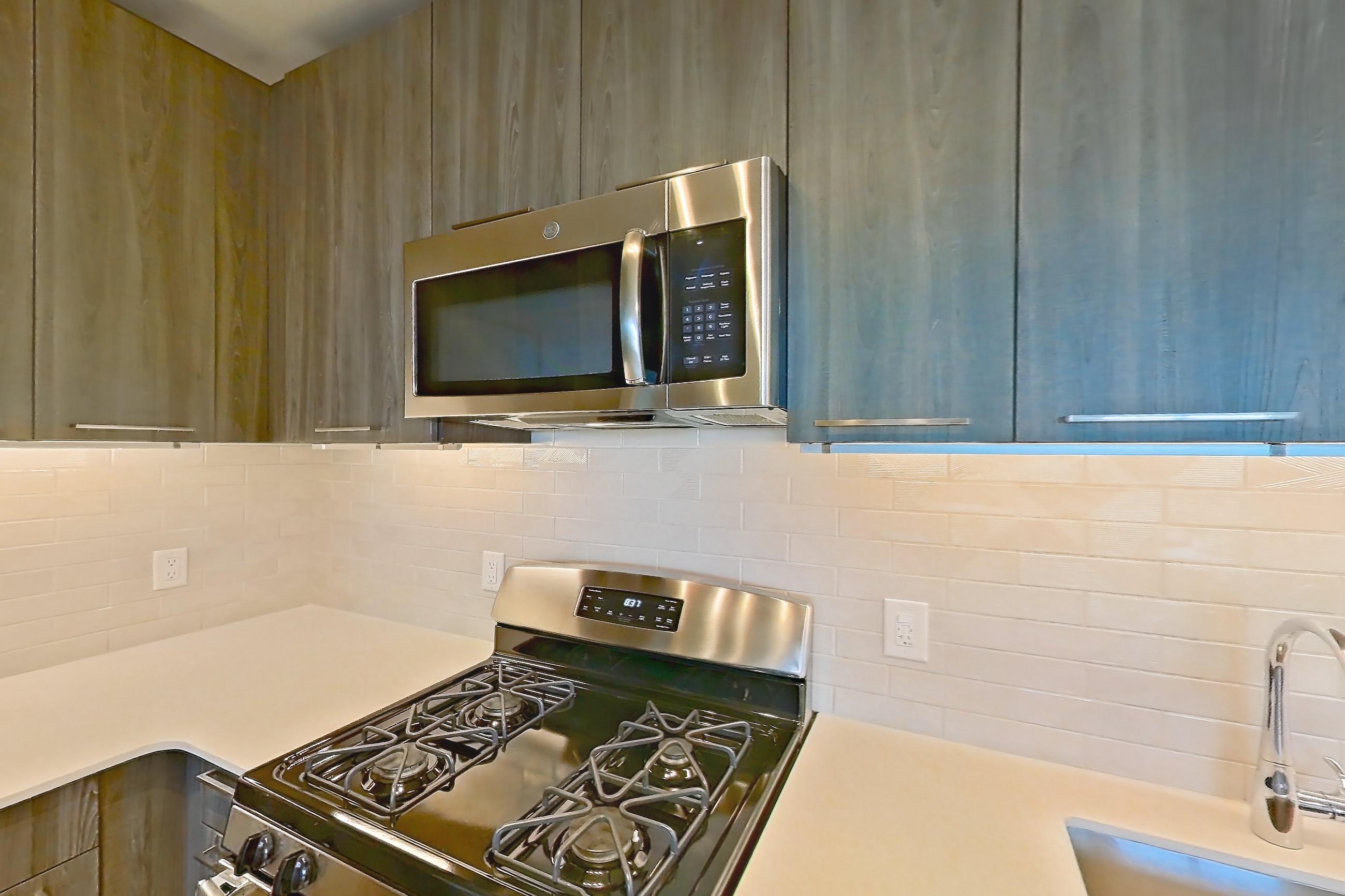 Kitchen with gas range, light countertops, light stone countertops, light wood-finish flooring, microwave, oven/range, refrigerator, and stainless steel appliances, Apartment 633S at Cortland Columbia Pike