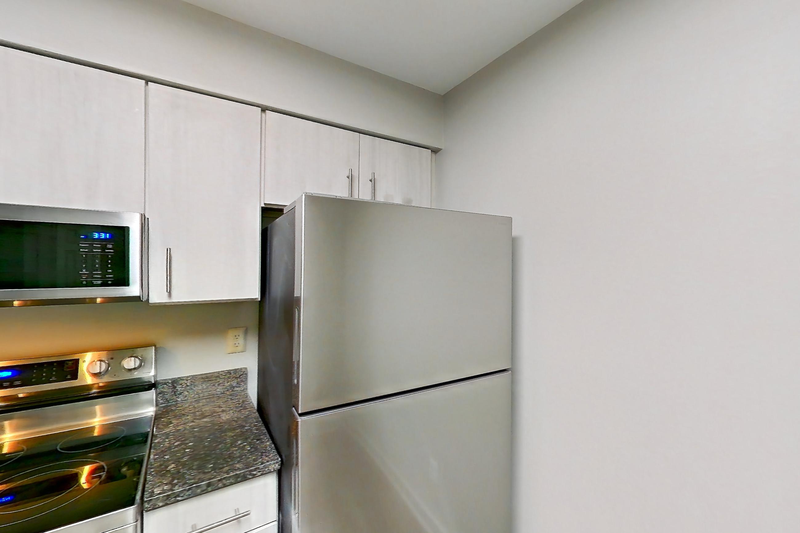 Kitchen with dark stone countertops, dishwasher, electric range, light wood-finish flooring, oven/range, range hood, refrigerator, and stainless steel appliances, Apartment 5812 at Cortland Manassas