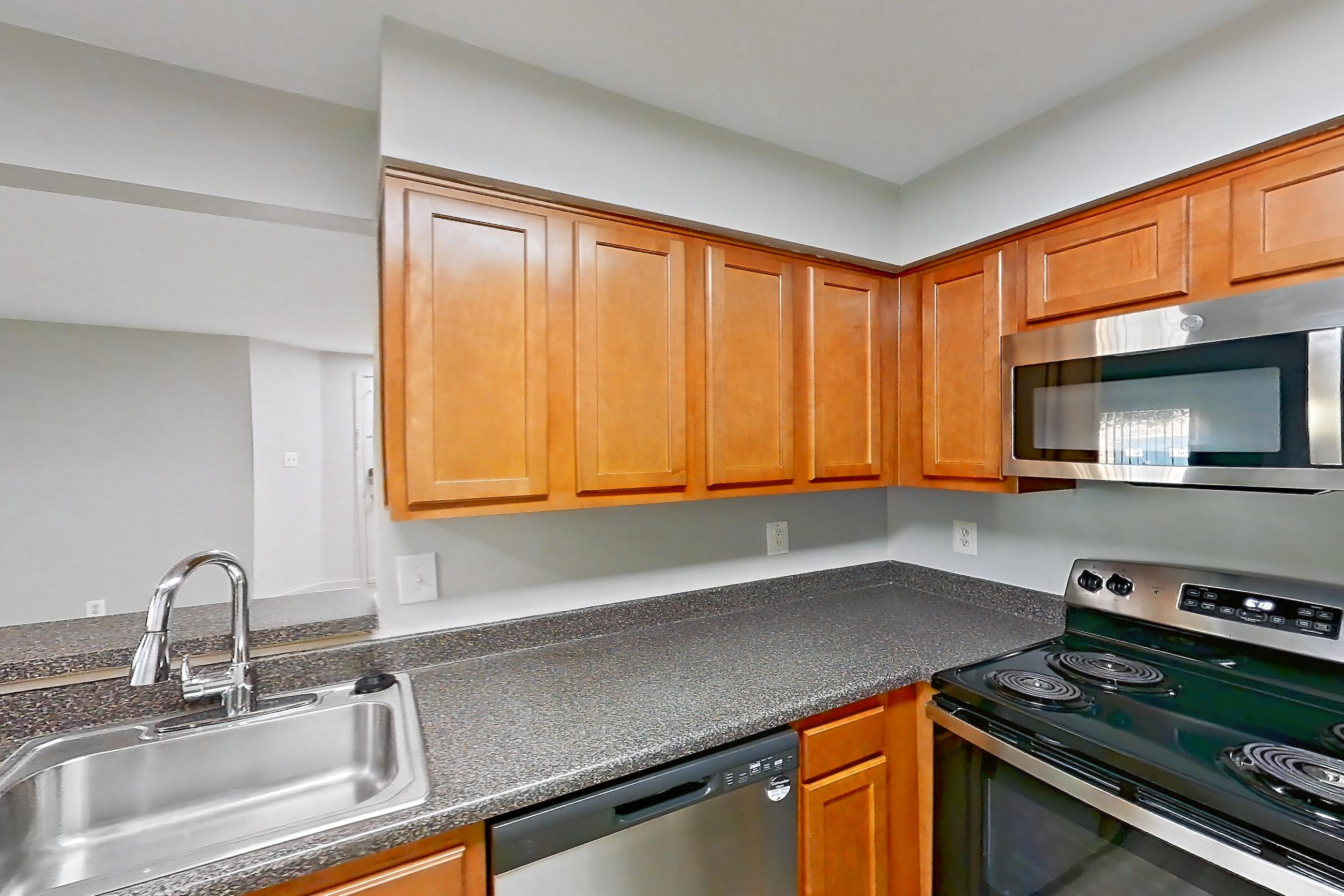 Kitchen with dark countertops, dishwasher, electric range, light countertops, light wood-finish flooring, microwave, oven/range, refrigerator, stainless steel appliances, and white appliances, Apartment 5612 at Cortland Manassas