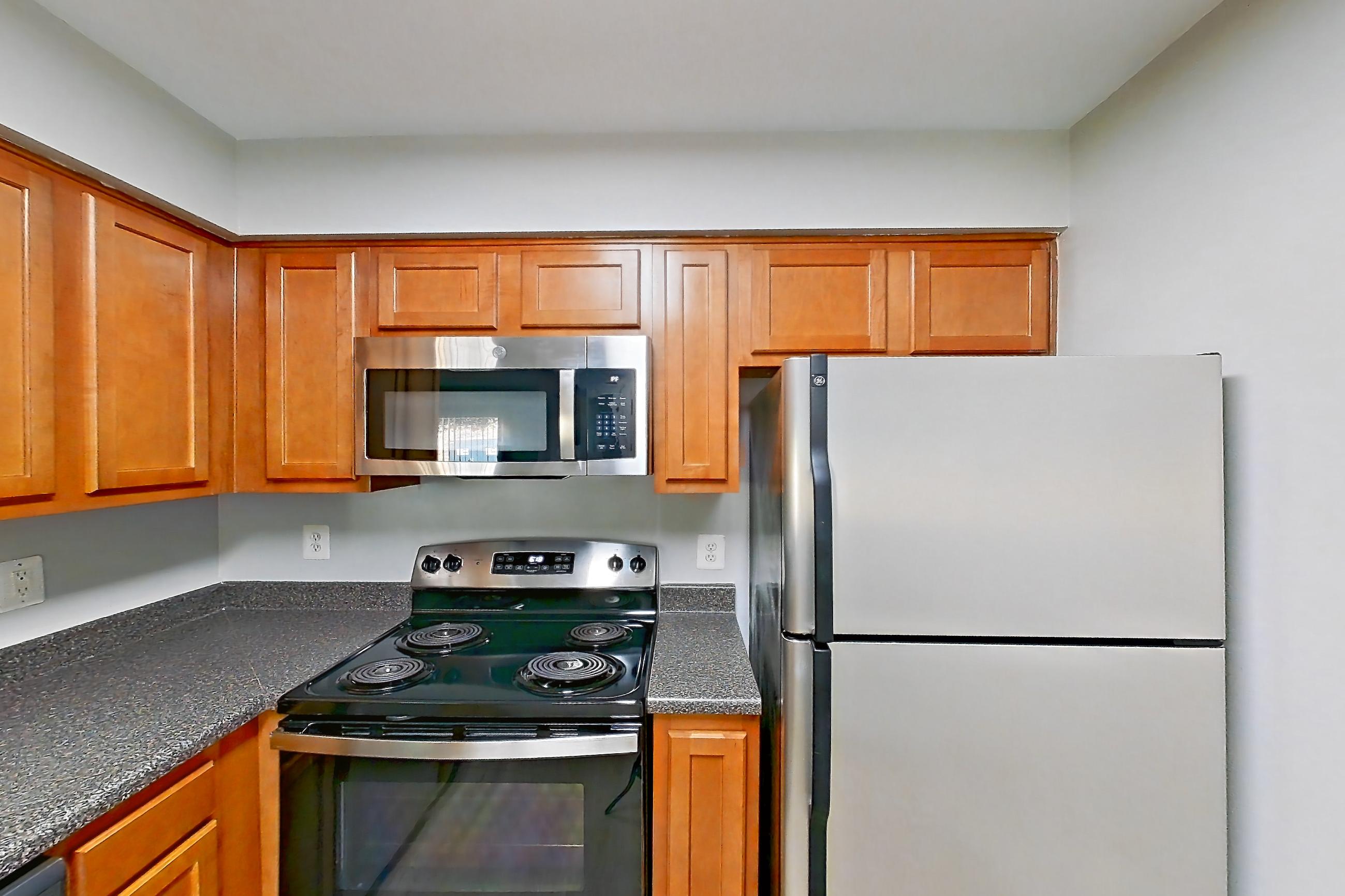 Kitchen with dark countertops, dishwasher, electric range, light countertops, light wood-finish flooring, microwave, oven/range, refrigerator, stainless steel appliances, and white appliances, Apartment 5612 at Cortland Manassas