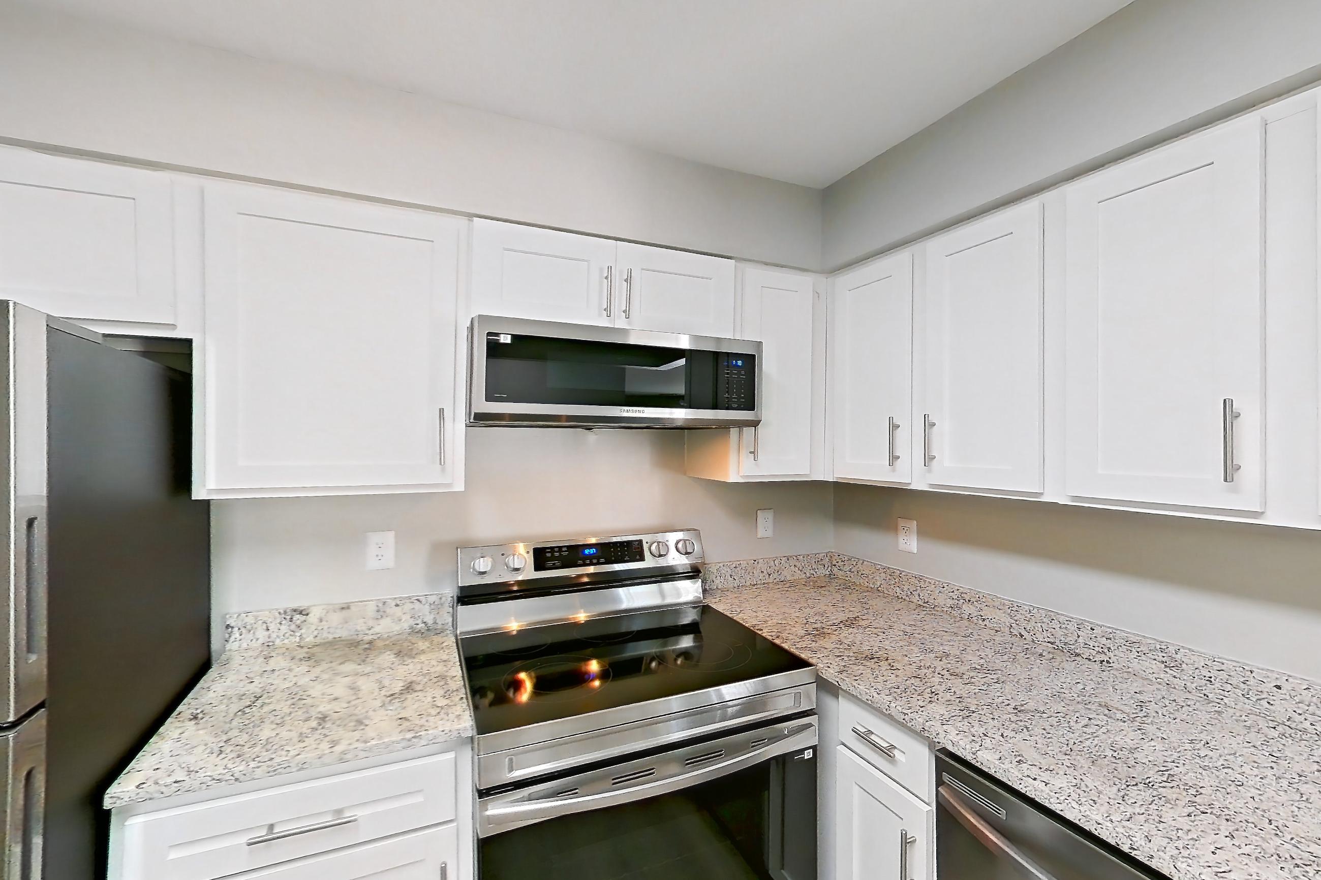 Kitchen with dishwasher, electric range, light countertops, light stone countertops, light wood-finish flooring, microwave, oven/range, refrigerator, and stainless steel appliances, Apartment 5421 at Cortland Manassas