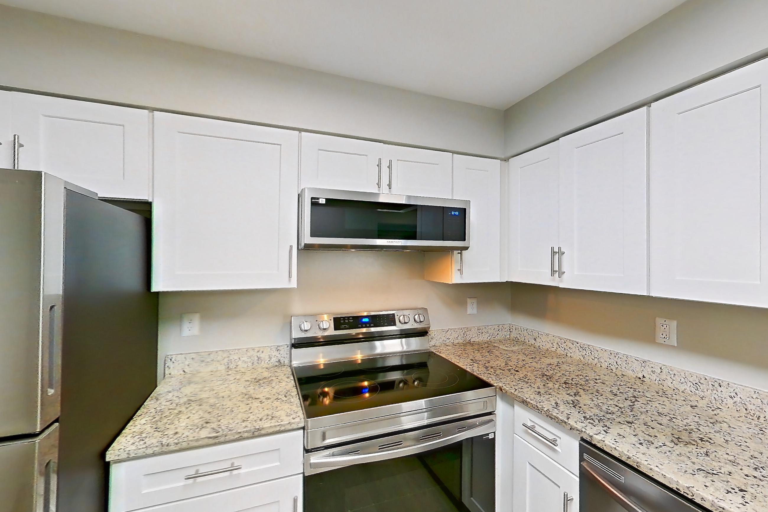 Kitchen with dishwasher, electric range, light countertops, light stone countertops, light wood-finish flooring, microwave, oven/range, refrigerator, and stainless steel appliances, Apartment 8521 at Cortland Manassas