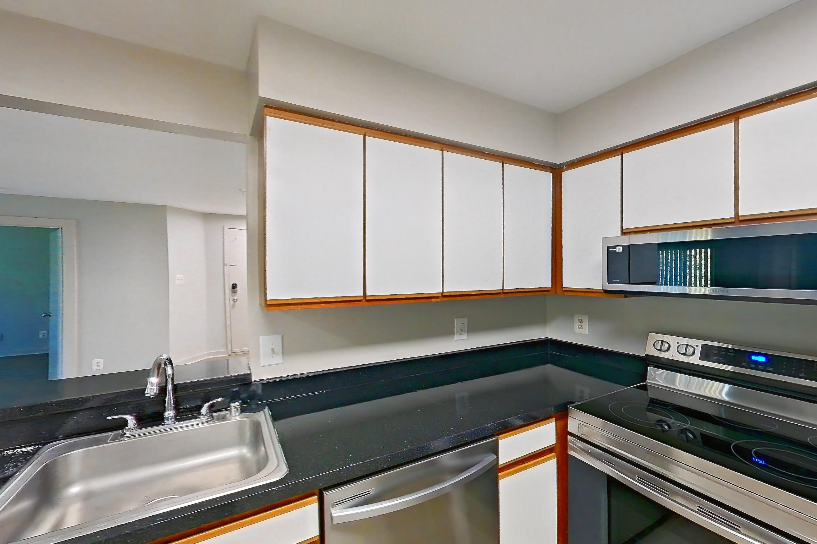 Kitchen with dark countertops, dark stone countertops, dishwasher, electric range, light wood-finish flooring, oven/range, refrigerator, and stainless steel appliances, Apartment 5022 at Cortland Manassas