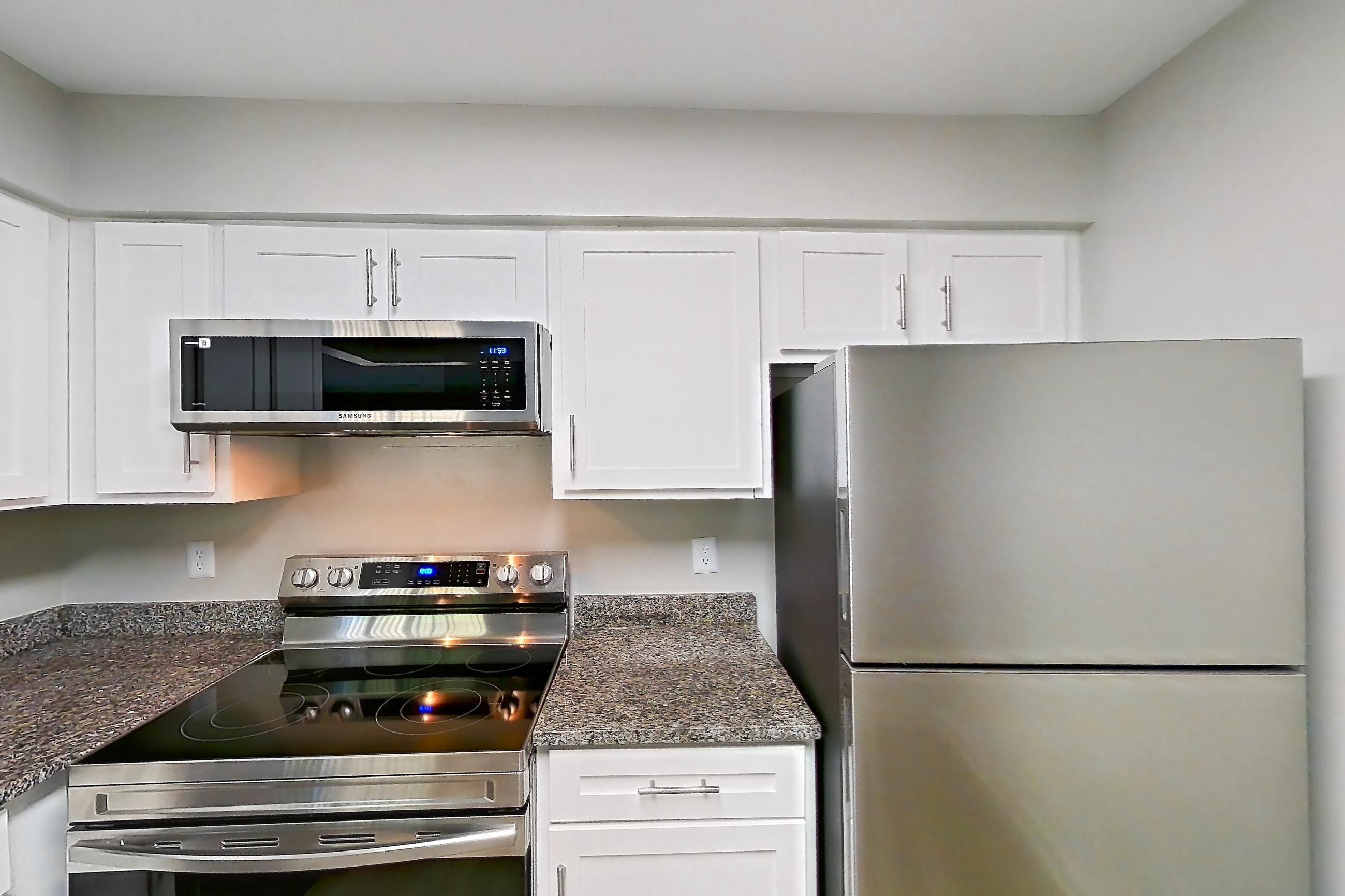 Kitchen with dark stone countertops, electric range, light wood-finish flooring, oven/range, refrigerator, and stainless steel appliances, Apartment 5422 at Cortland Manassas