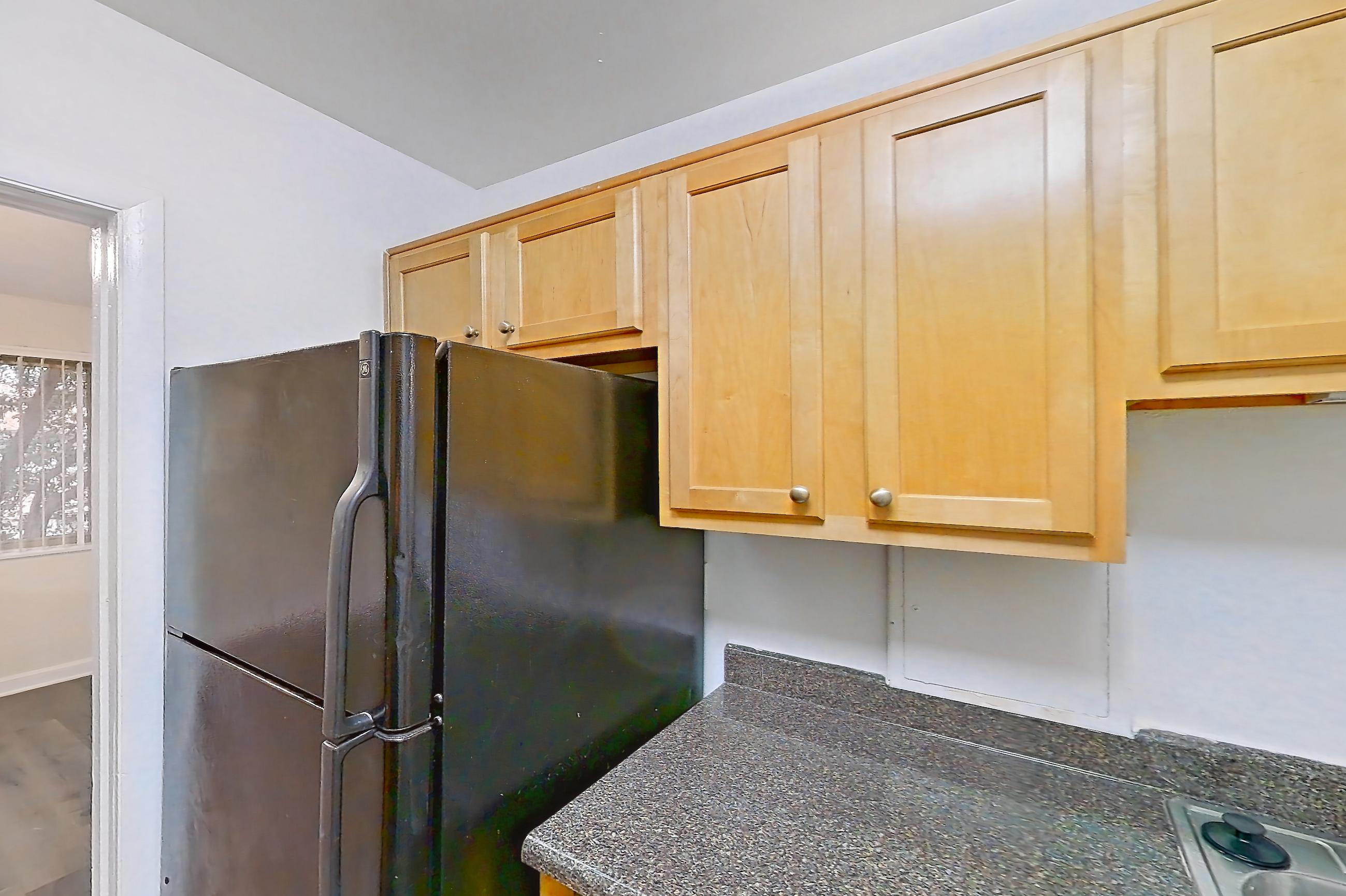 Kitchen with black appliances, dark countertops, dark stone countertops, dark wood-finish flooring, dishwasher, gas range, light countertops, microwave, oven/range, refrigerator, and stainless steel appliances, Apartment C-402 at Cortland on Pike