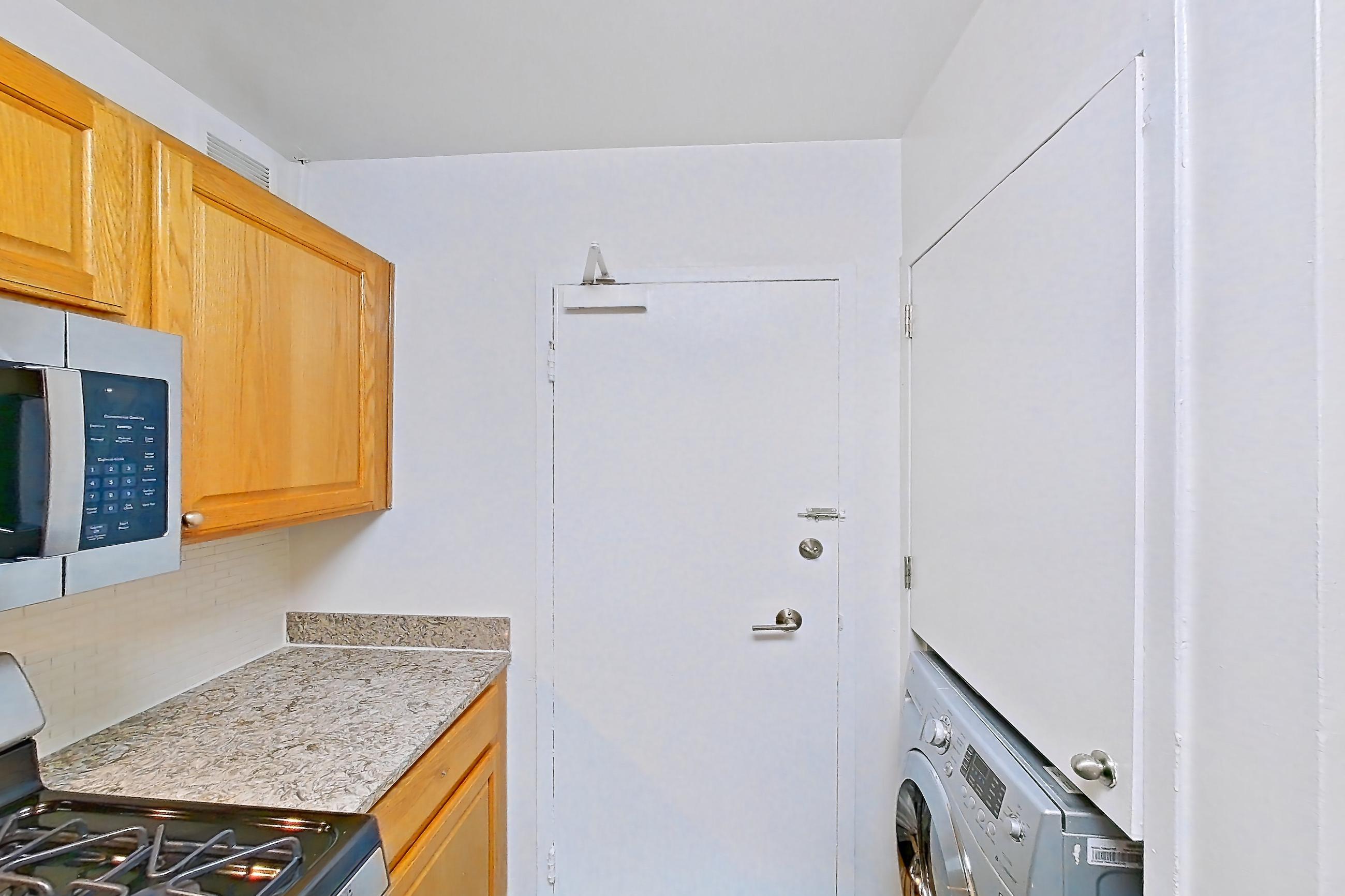 Kitchen with dishwasher, gas range, in-unit laundry, light countertops, light stone countertops, light wood-finish flooring, microwave, oven/range, refrigerator, and stainless steel appliances, Apartment C-209 at Cortland on Pike