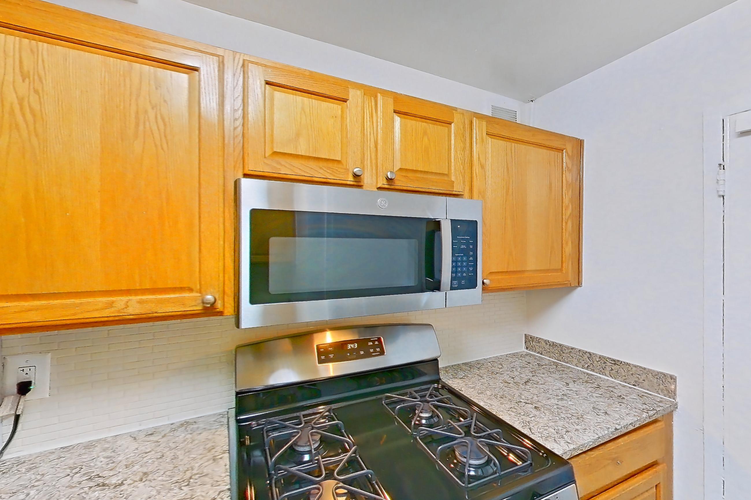 Kitchen with dishwasher, gas range, in-unit laundry, light countertops, light stone countertops, light wood-finish flooring, microwave, oven/range, refrigerator, and stainless steel appliances, Apartment C-209 at Cortland on Pike
