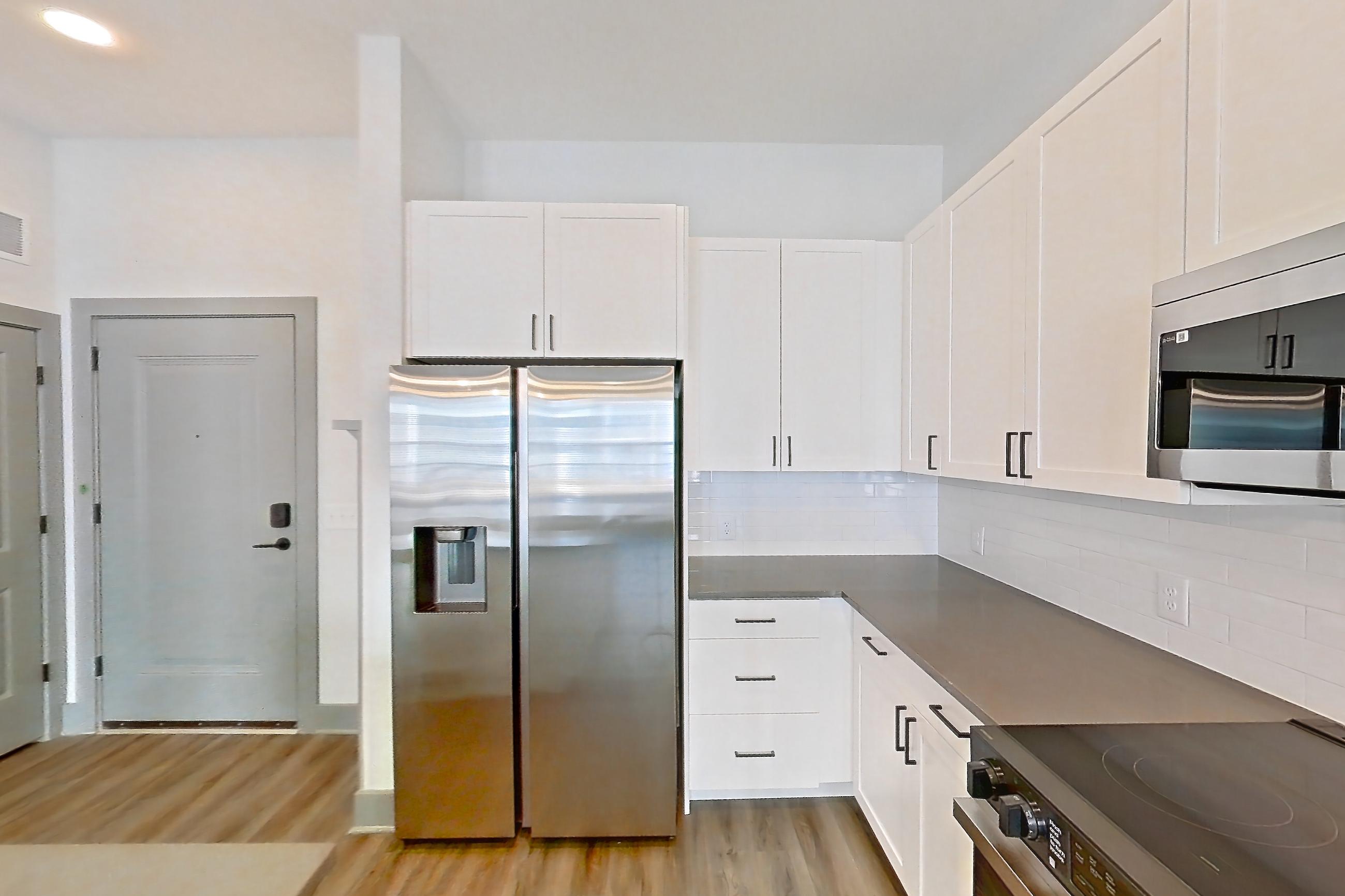 Kitchen with dark countertops, dark wood-finish flooring, electric range, light countertops, light stone countertops, light wood-finish flooring, microwave, oven/range, refrigerator, stainless steel appliances, and water & ice dispenser, Apartment 4106 at District Eastside