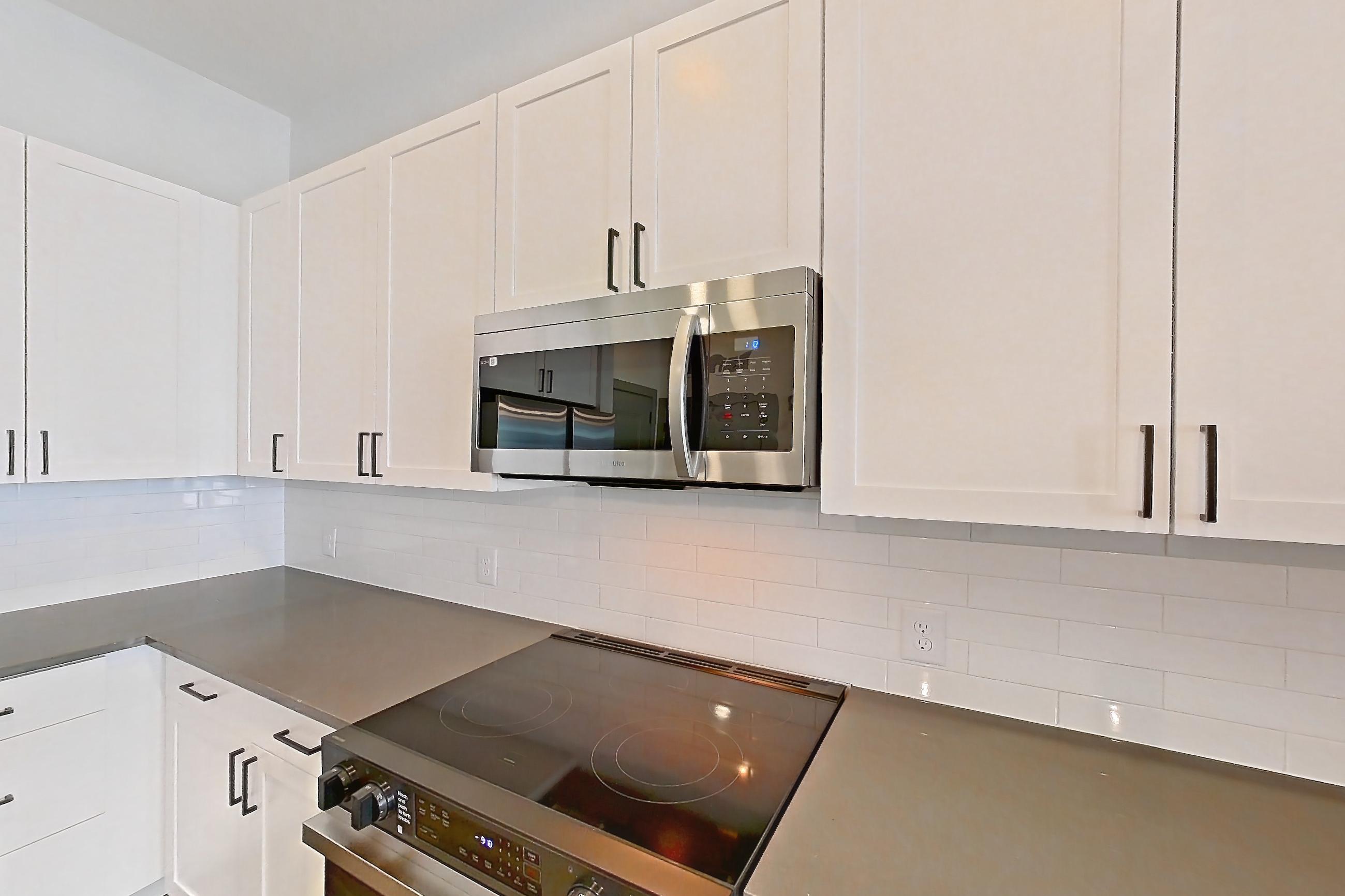 Kitchen with dark countertops, dark wood-finish flooring, electric range, light countertops, light stone countertops, light wood-finish flooring, microwave, oven/range, refrigerator, stainless steel appliances, and water & ice dispenser, Apartment 4106 at District Eastside