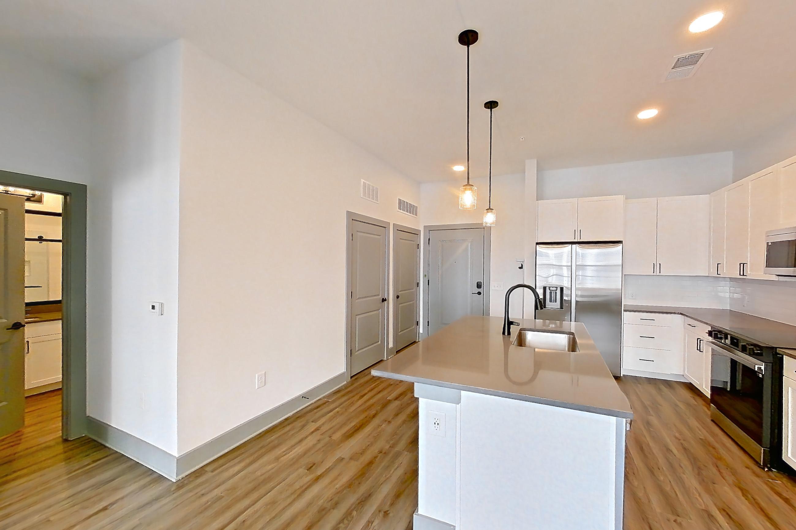 Living space with dark countertops, dark wood-finish flooring, electric range, kitchen island, light stone countertops, light wood-finish flooring, oven/range, refrigerator, stainless steel appliances, and water & ice dispenser, Apartment 4106 at District Eastside