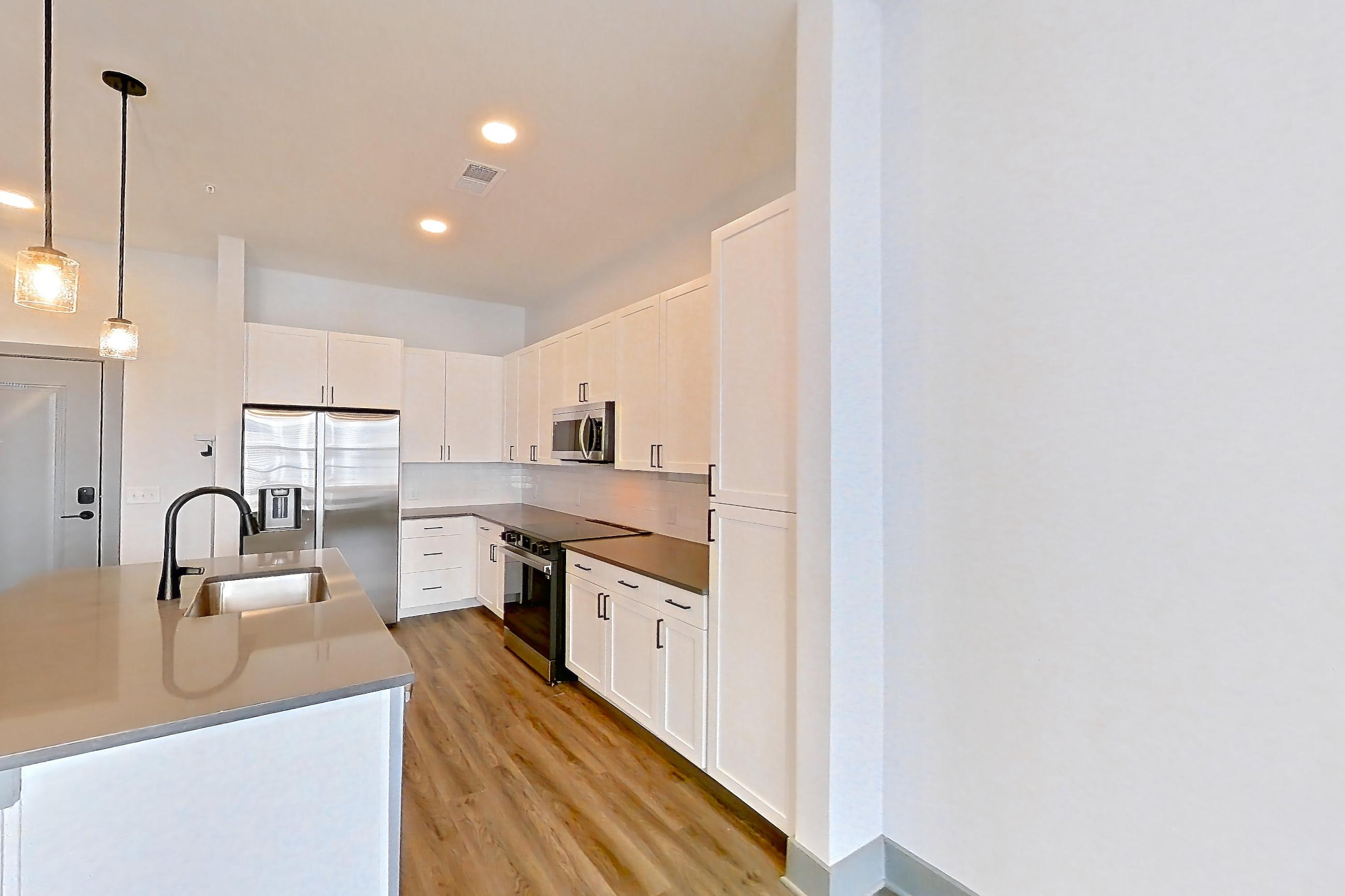 Living space with dark countertops, dark wood-finish flooring, electric range, kitchen island, light stone countertops, light wood-finish flooring, oven/range, refrigerator, stainless steel appliances, and water & ice dispenser, Apartment 4106 at District Eastside