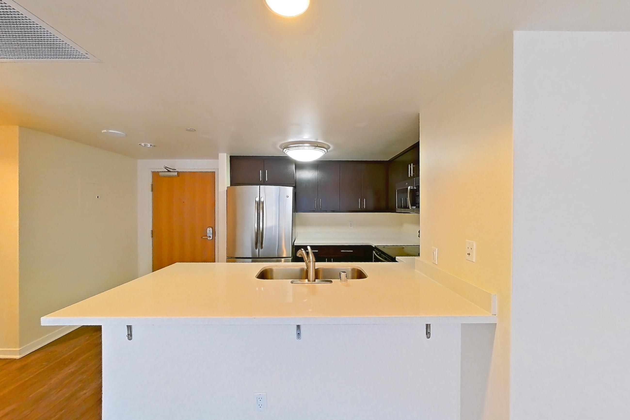 Dining room with dark wood-finish flooring, electric range, light countertops, microwave, refrigerator, and stainless steel appliances, Apartment 1008 at The Towers at Rincon Apartments