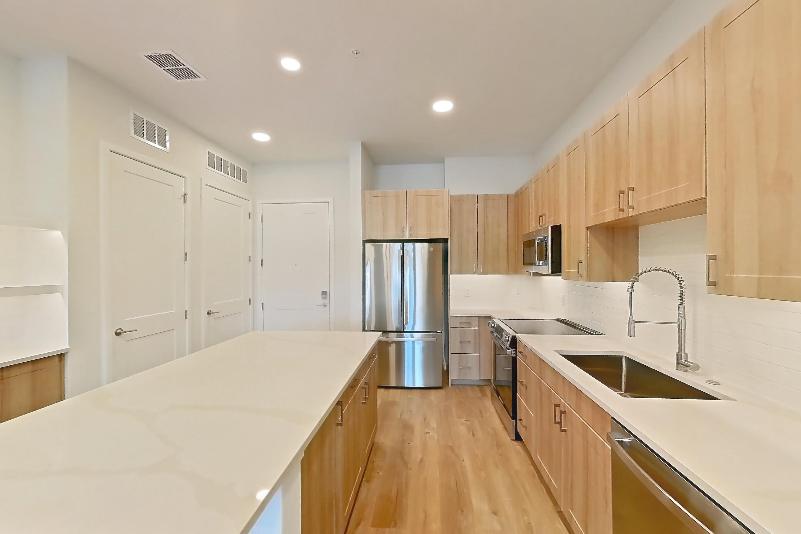 Kitchen with dishwasher, electric range, light countertops, light stone countertops, light wood-finish flooring, microwave, oven/range, refrigerator, and stainless steel appliances, Apartment 115 at Lantower Bayside