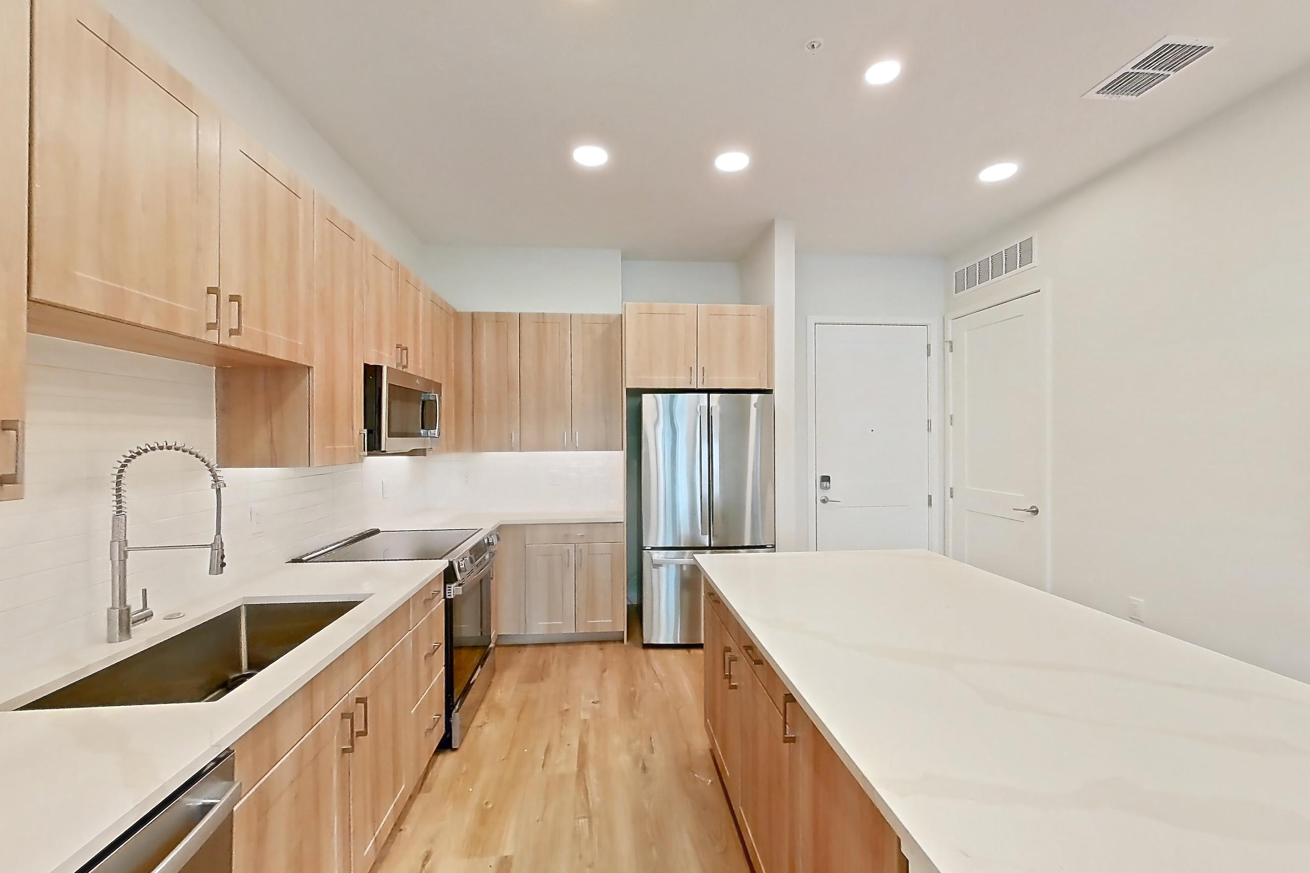 Kitchen with dishwasher, electric range, light countertops, light stone countertops, light wood-finish flooring, microwave, oven/range, refrigerator, and stainless steel appliances, Apartment 156 at Lantower Bayside