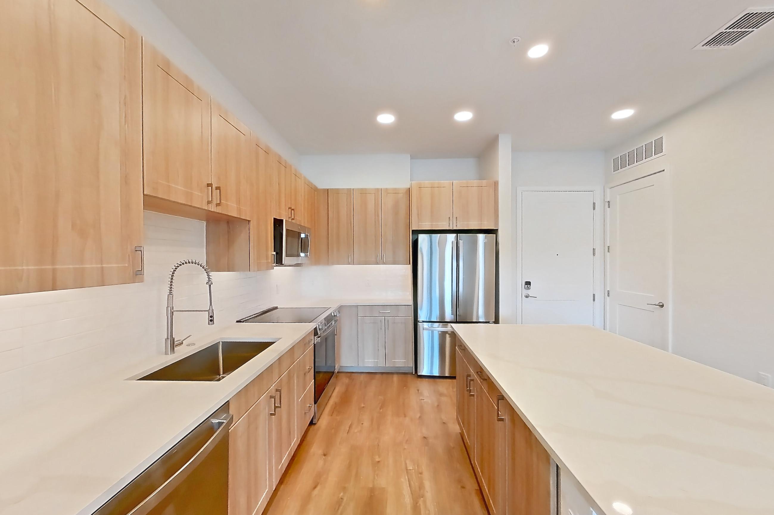 Kitchen with dishwasher, electric range, light countertops, light stone countertops, light wood-finish flooring, microwave, oven/range, refrigerator, and stainless steel appliances, Apartment 233 at Lantower Bayside
