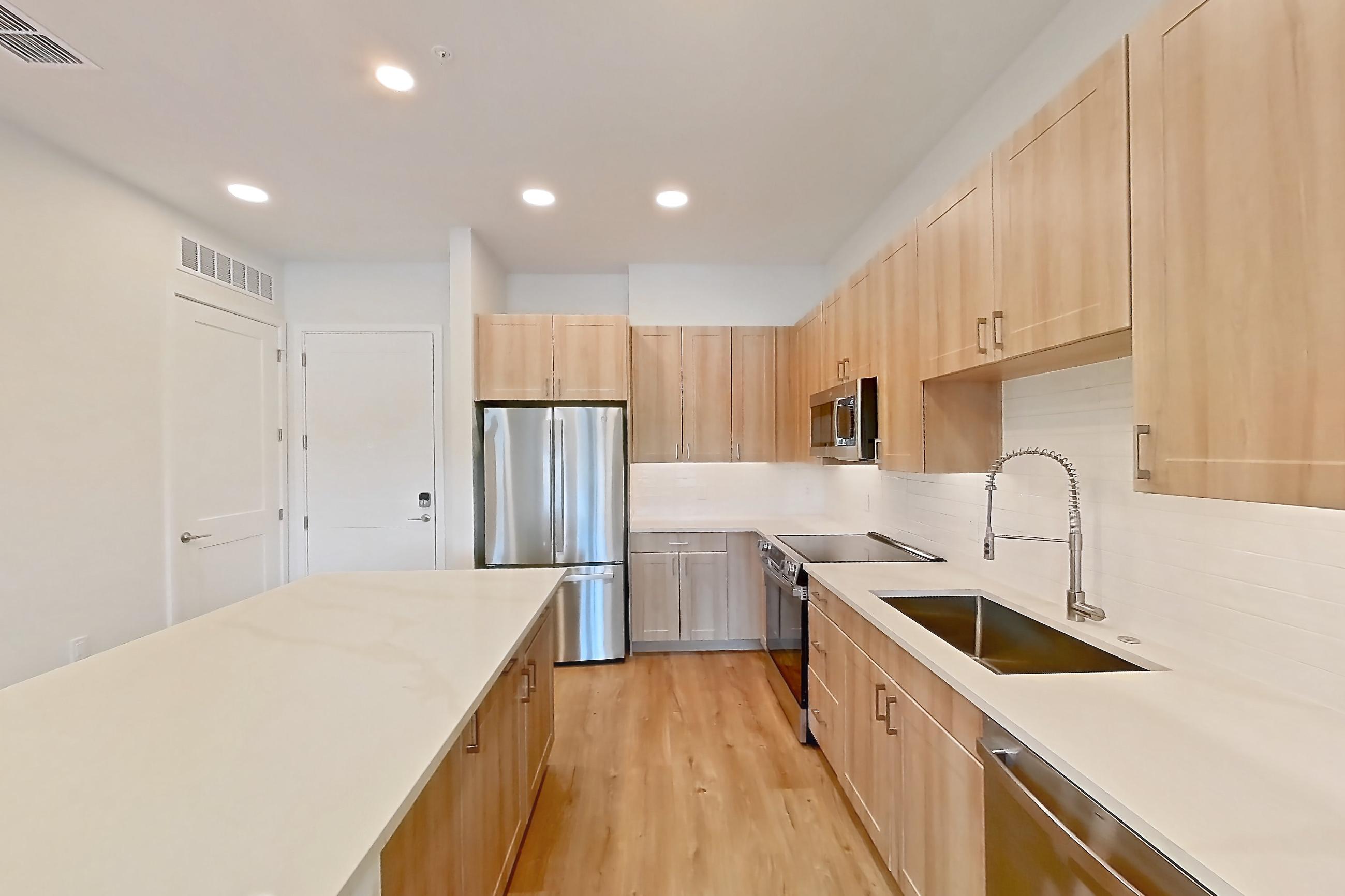 Kitchen with dishwasher, electric range, light countertops, light stone countertops, light wood-finish flooring, microwave, oven/range, refrigerator, and stainless steel appliances, Apartment 235 at Lantower Bayside