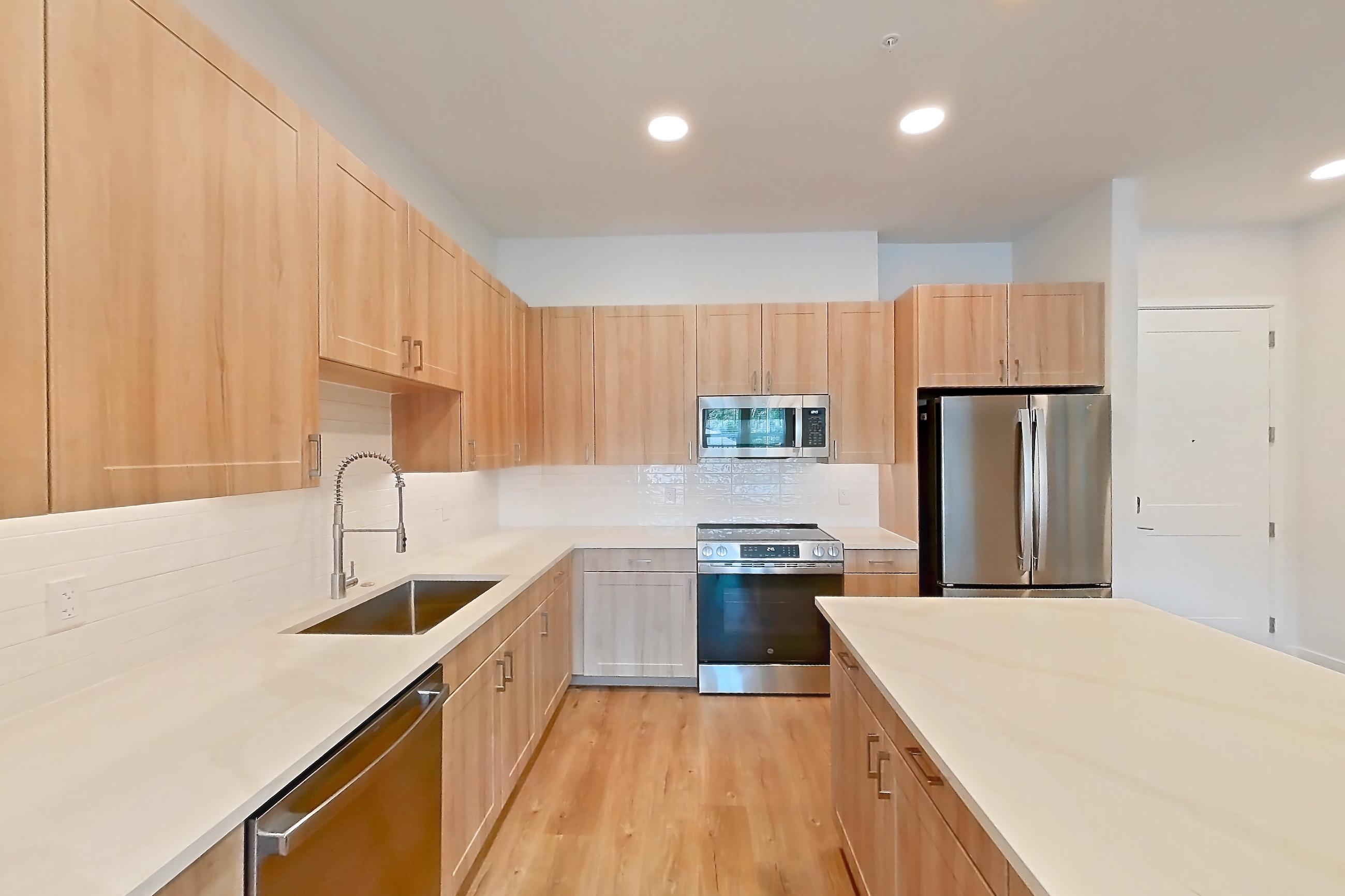 Kitchen with dishwasher, electric range, light countertops, light stone countertops, light wood-finish flooring, microwave, oven/range, refrigerator, and stainless steel appliances, Apartment 239 at Lantower Bayside