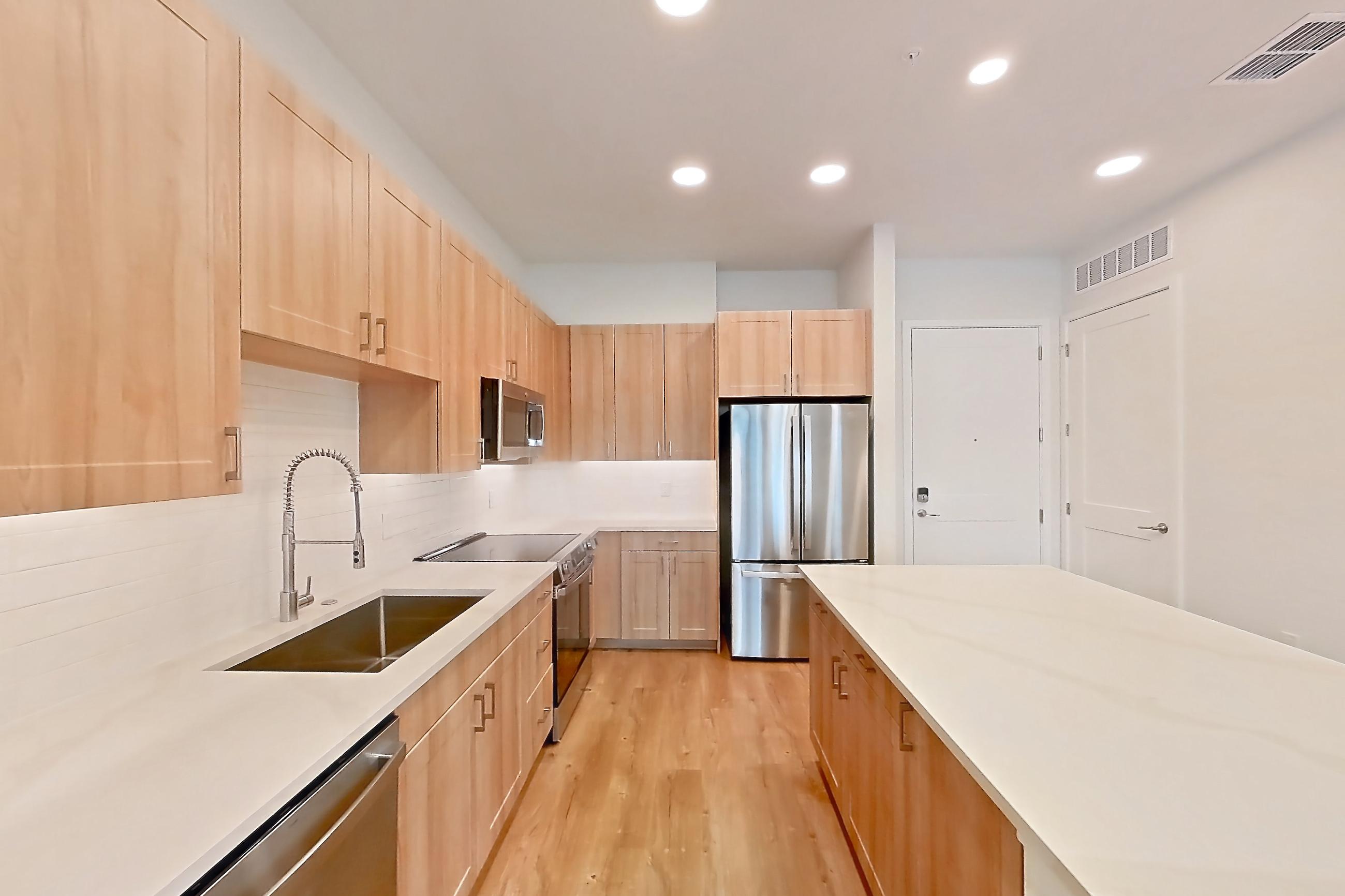 Kitchen with dishwasher, electric range, light countertops, light stone countertops, light wood-finish flooring, microwave, oven/range, refrigerator, and stainless steel appliances, Apartment 240 at Lantower Bayside