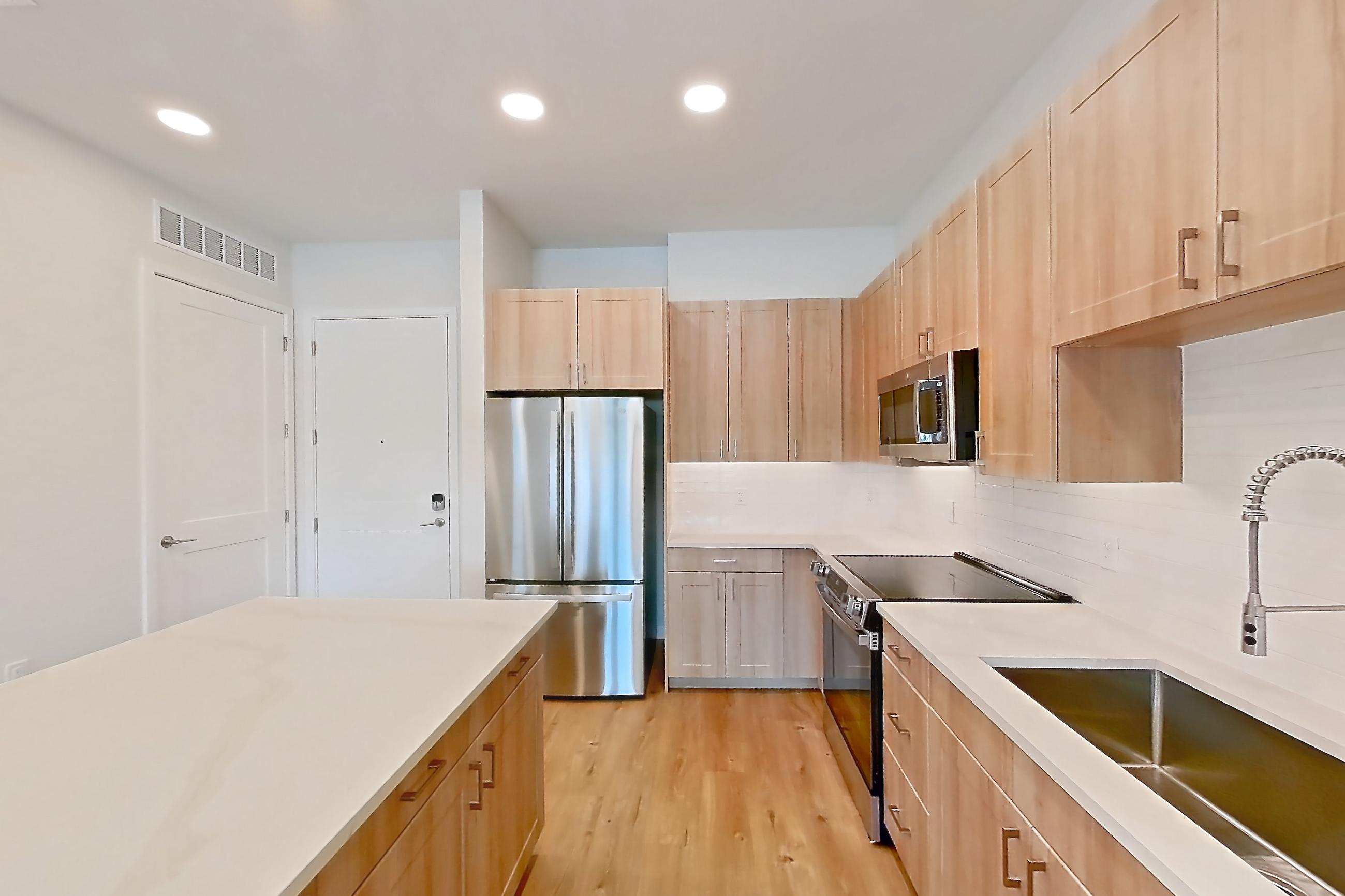 Kitchen with dishwasher, electric range, light countertops, light stone countertops, light wood-finish flooring, microwave, oven/range, refrigerator, and stainless steel appliances, Apartment 241 at Lantower Bayside
