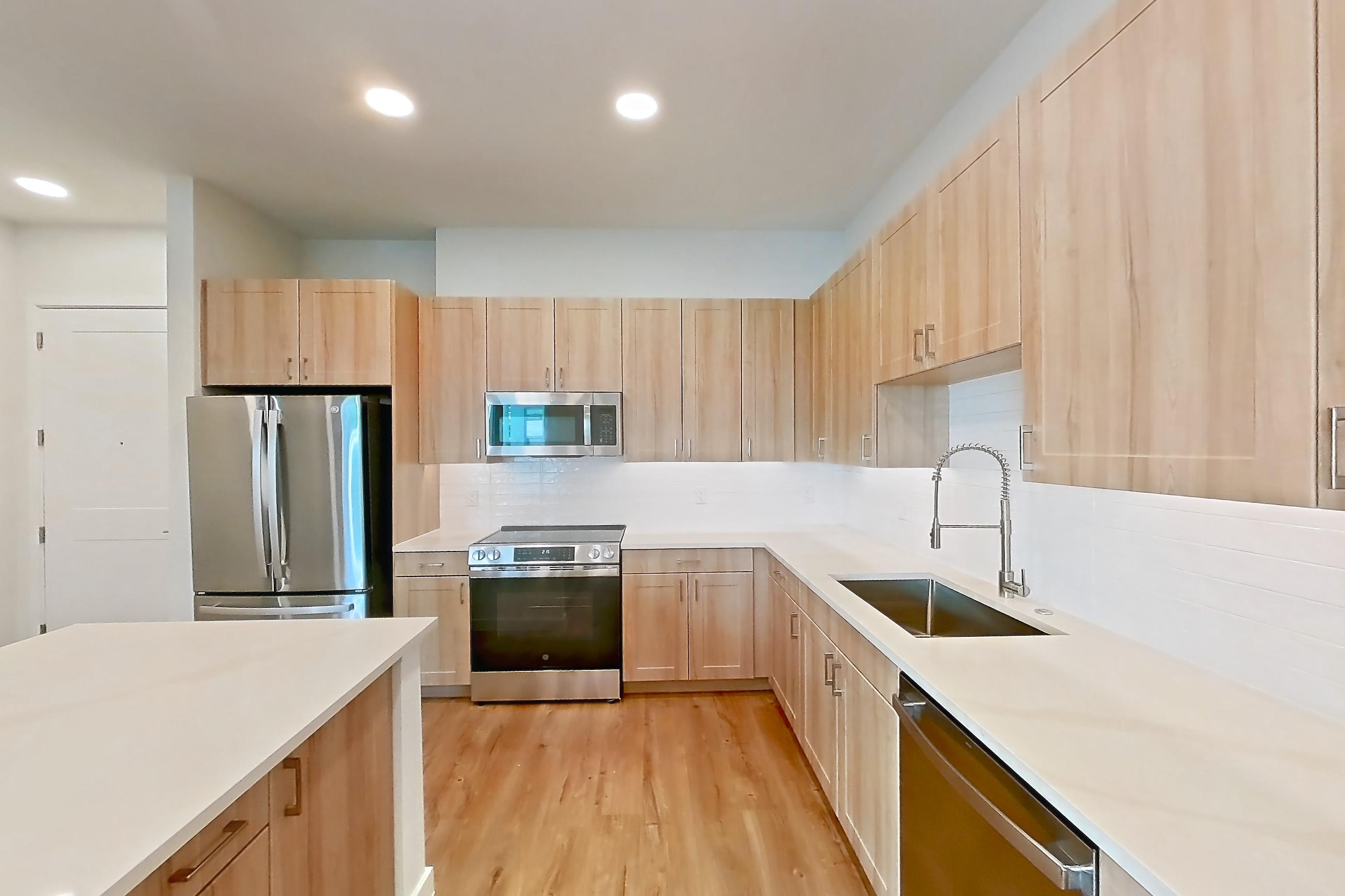 Kitchen with dishwasher, electric range, light countertops, light stone countertops, light wood-finish flooring, microwave, oven/range, refrigerator, and stainless steel appliances, Apartment 242 at Lantower Bayside