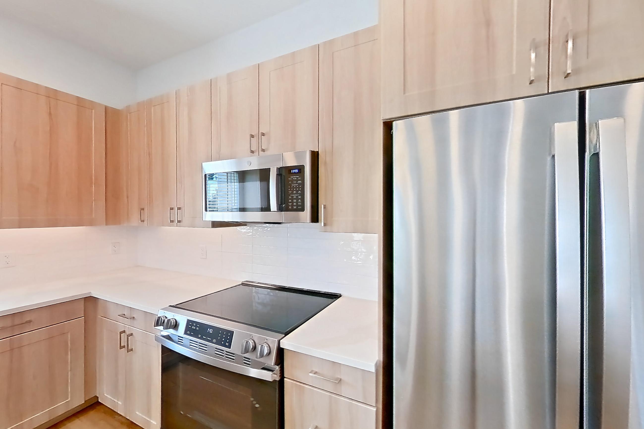 Kitchen with dishwasher, electric range, light countertops, light stone countertops, light wood-finish flooring, microwave, oven/range, refrigerator, and stainless steel appliances, Apartment 243 at Lantower Bayside