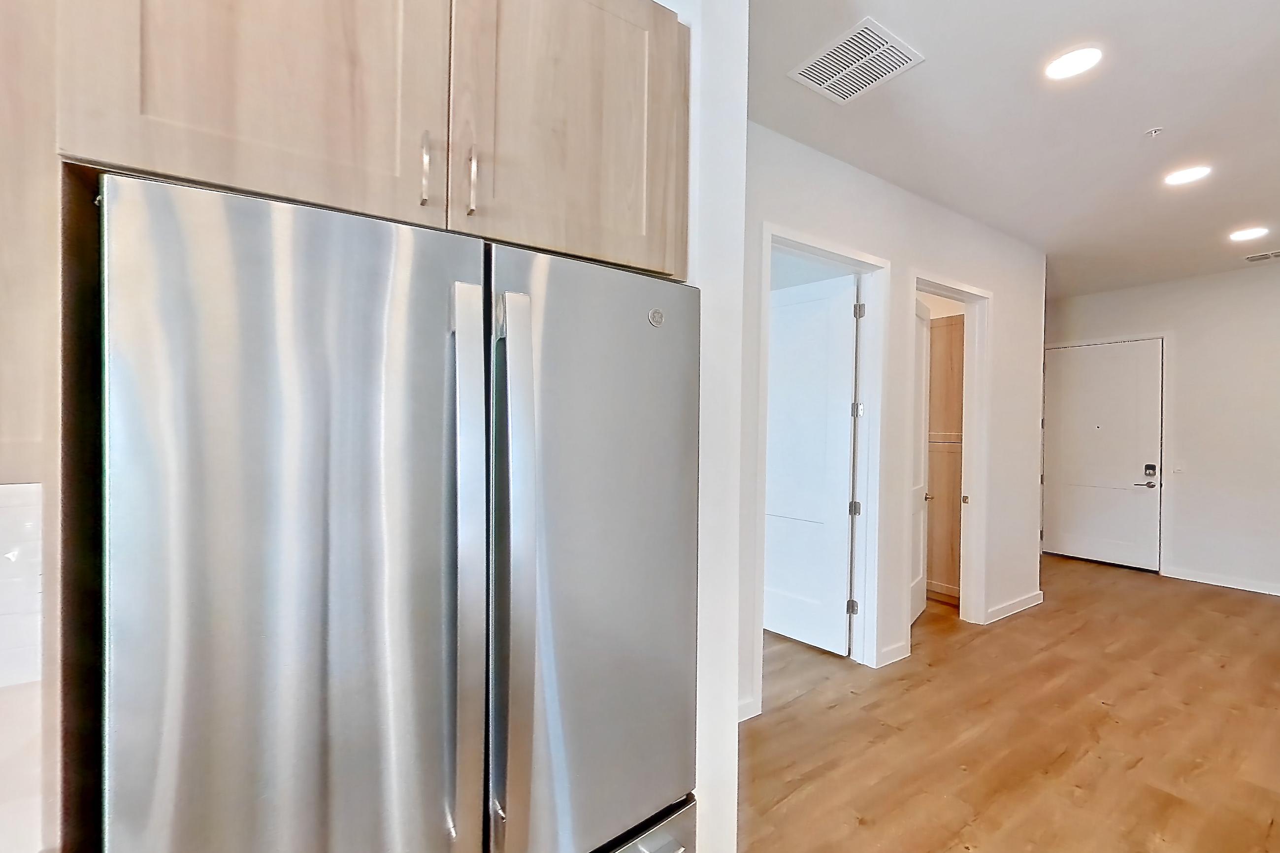 Kitchen with dishwasher, electric range, light countertops, light stone countertops, light wood-finish flooring, microwave, oven/range, refrigerator, and stainless steel appliances, Apartment 243 at Lantower Bayside
