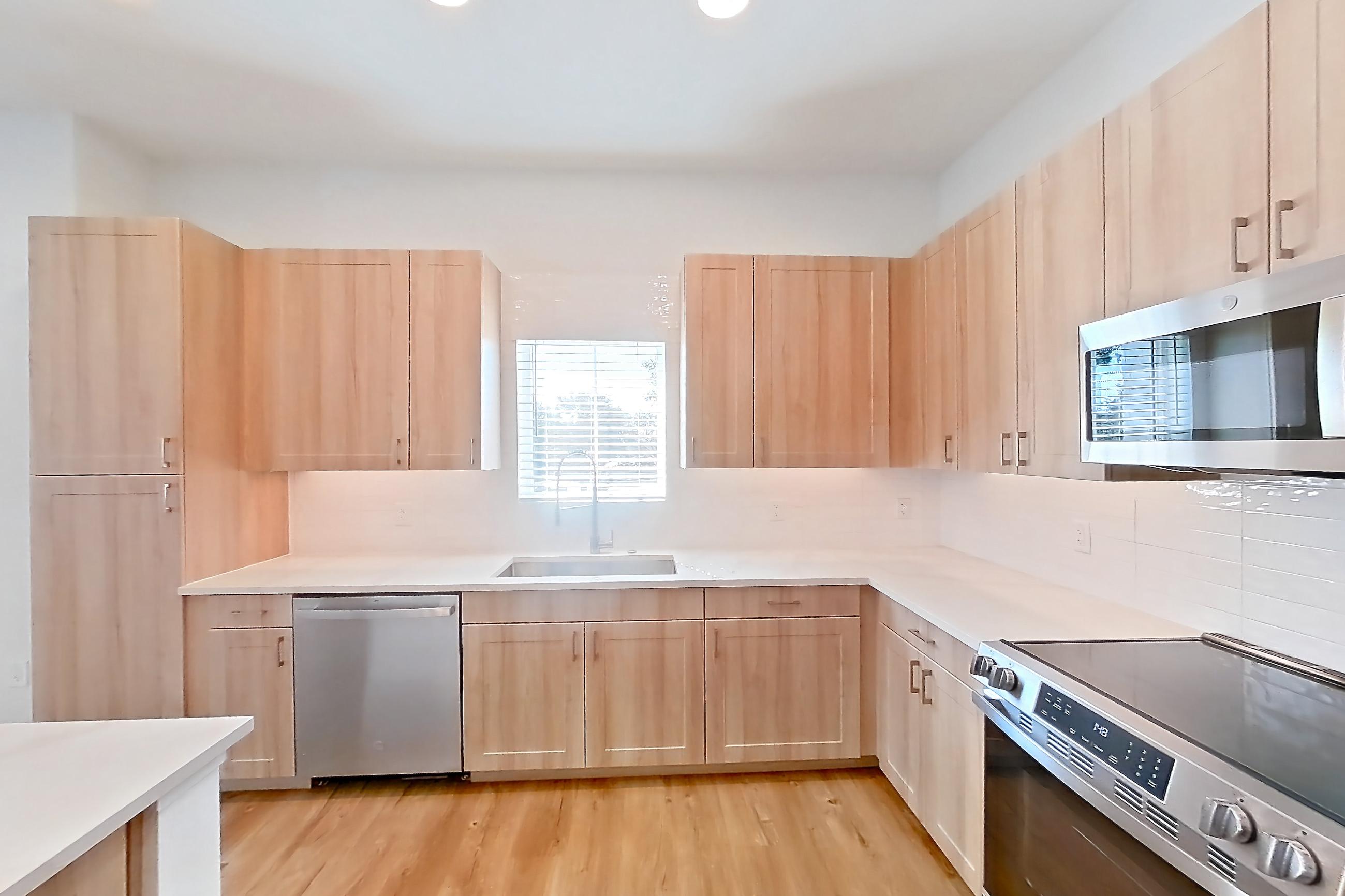 Kitchen with dishwasher, electric range, light countertops, light stone countertops, light wood-finish flooring, microwave, oven/range, refrigerator, and stainless steel appliances, Apartment 243 at Lantower Bayside