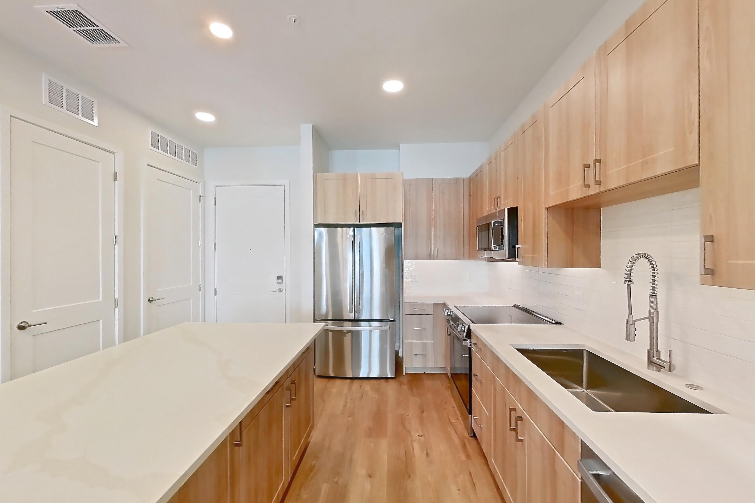 Kitchen with dishwasher, electric range, light countertops, light stone countertops, light wood-finish flooring, microwave, oven/range, refrigerator, and stainless steel appliances, Apartment 248 at Lantower Bayside